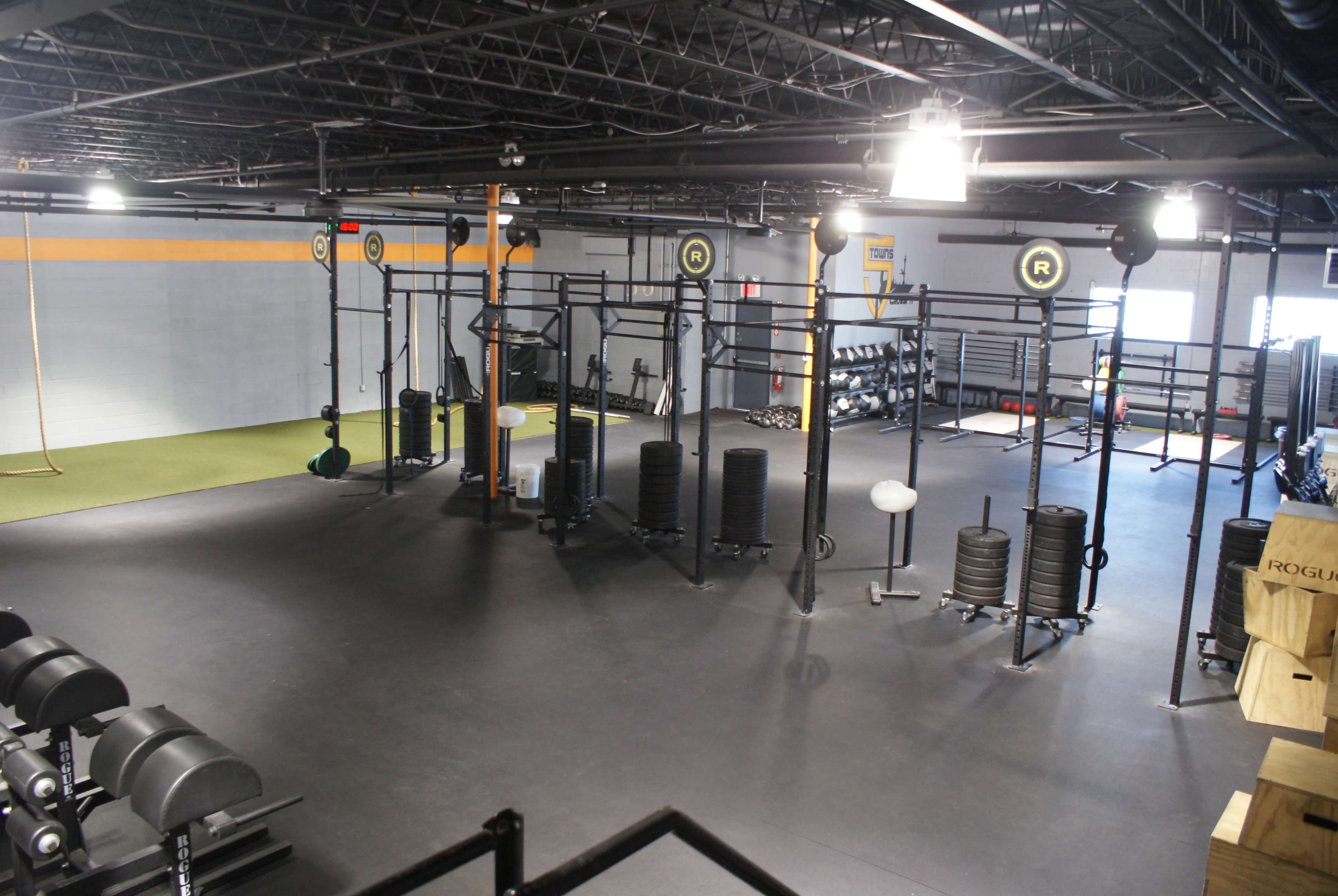 The image shows a spacious gym area equipped with various weightlifting and exercise equipment organized on the floor.