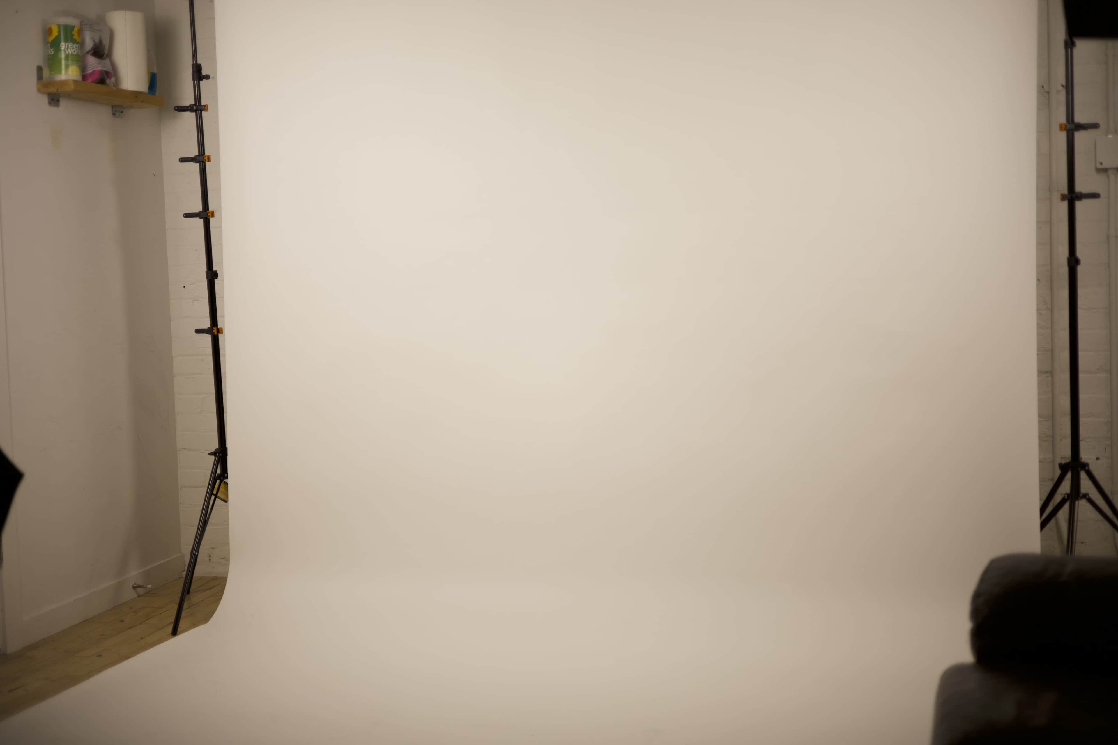 The image shows a minimalistic photo studio with a plain, light-colored backdrop and two light stands.