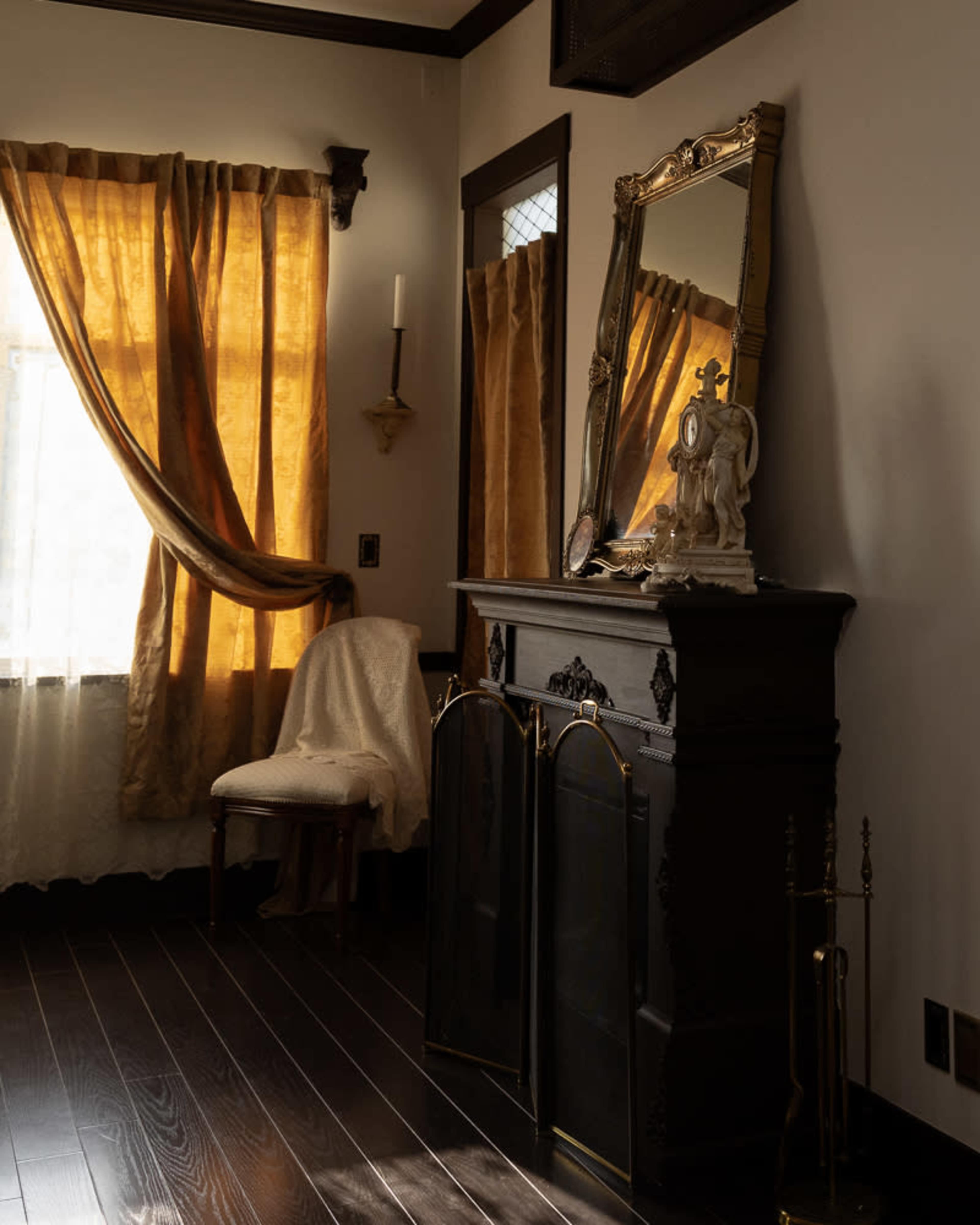 A dark wooden fireplace with decorative elements stands against a wall, flanked by long, flowing gold curtains and a large mirror above it.