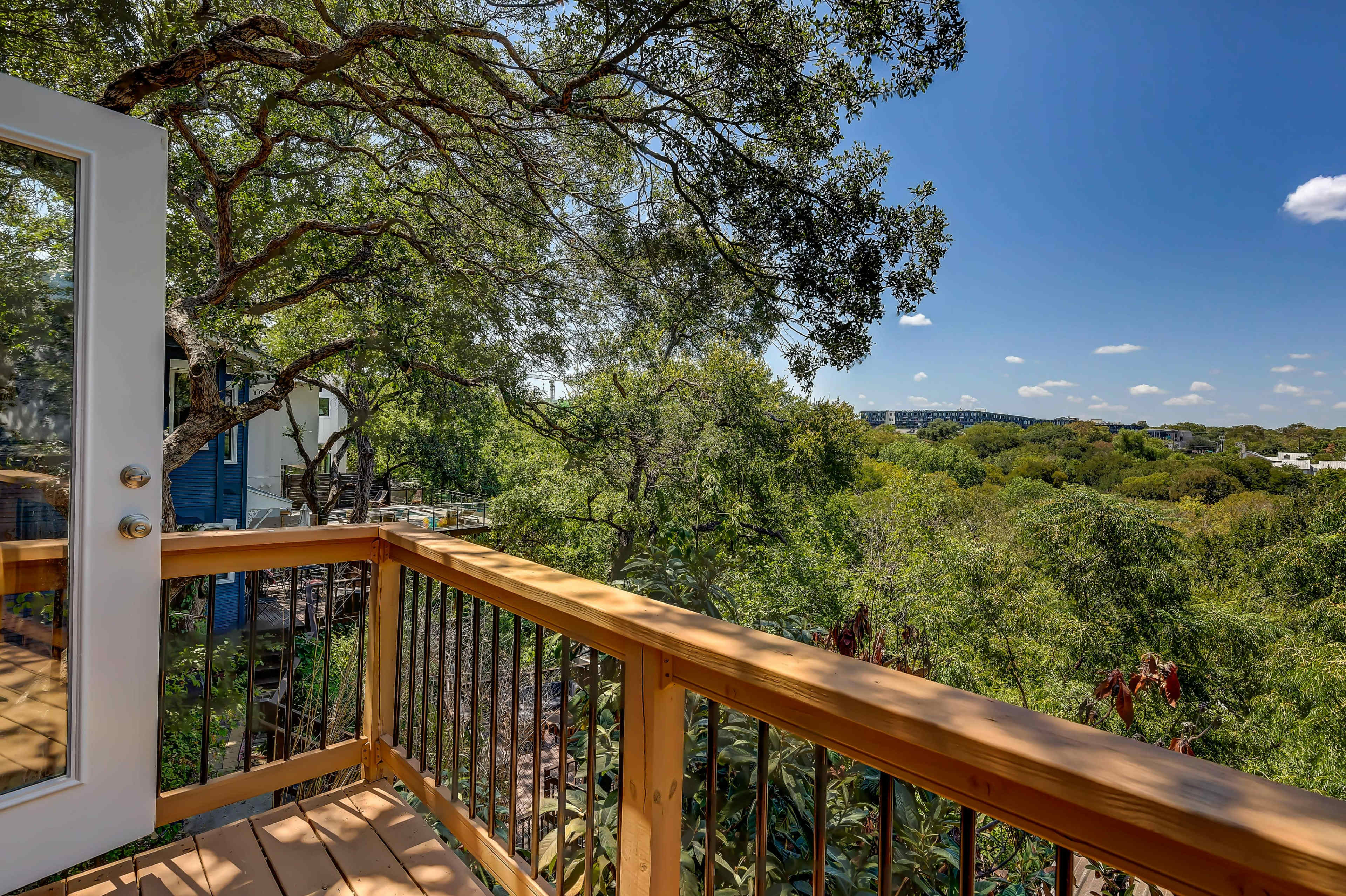 A wooden balcony overlooks a lush, green landscape under a clear blue sky.
