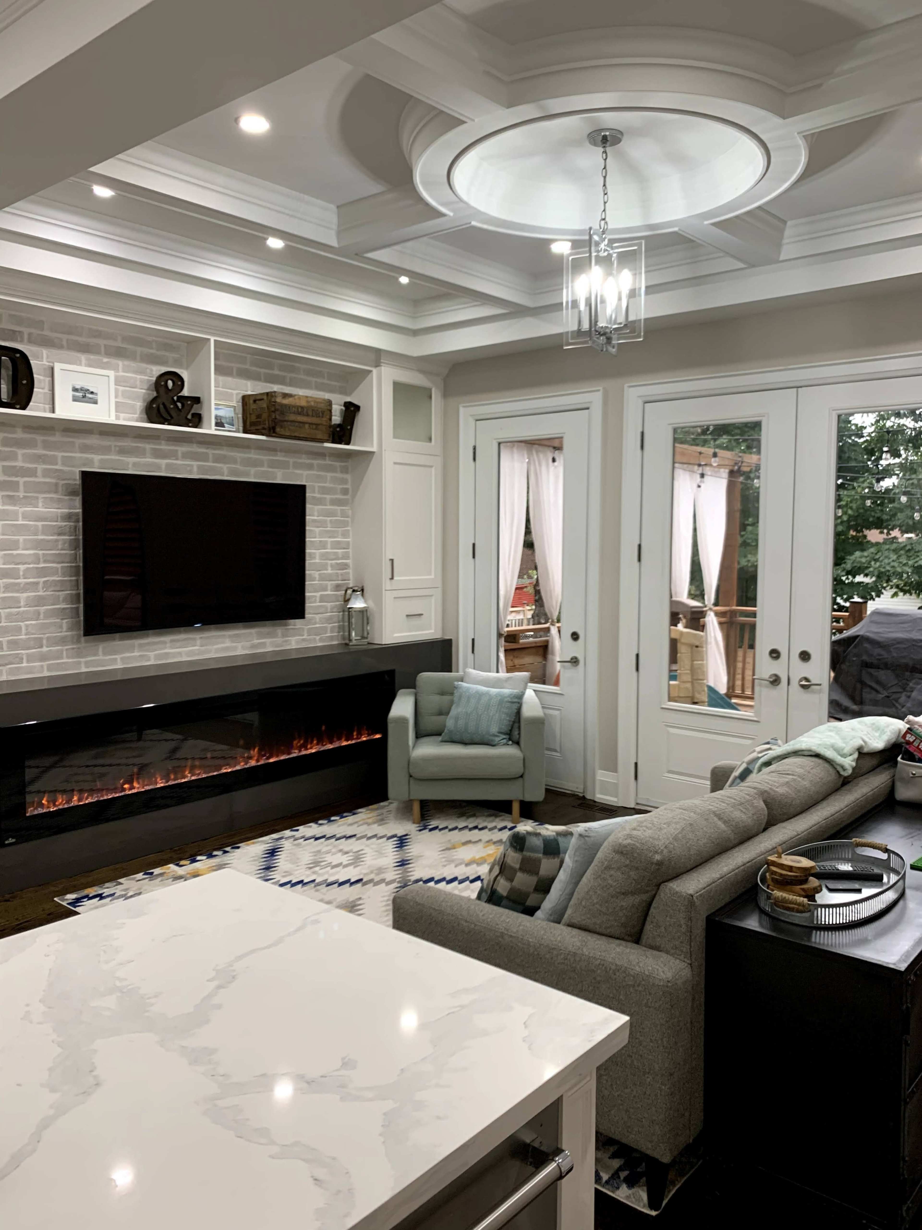 A modern living room with a fireplace, a television mounted on the wall, and large glass doors leading to an outdoor area.