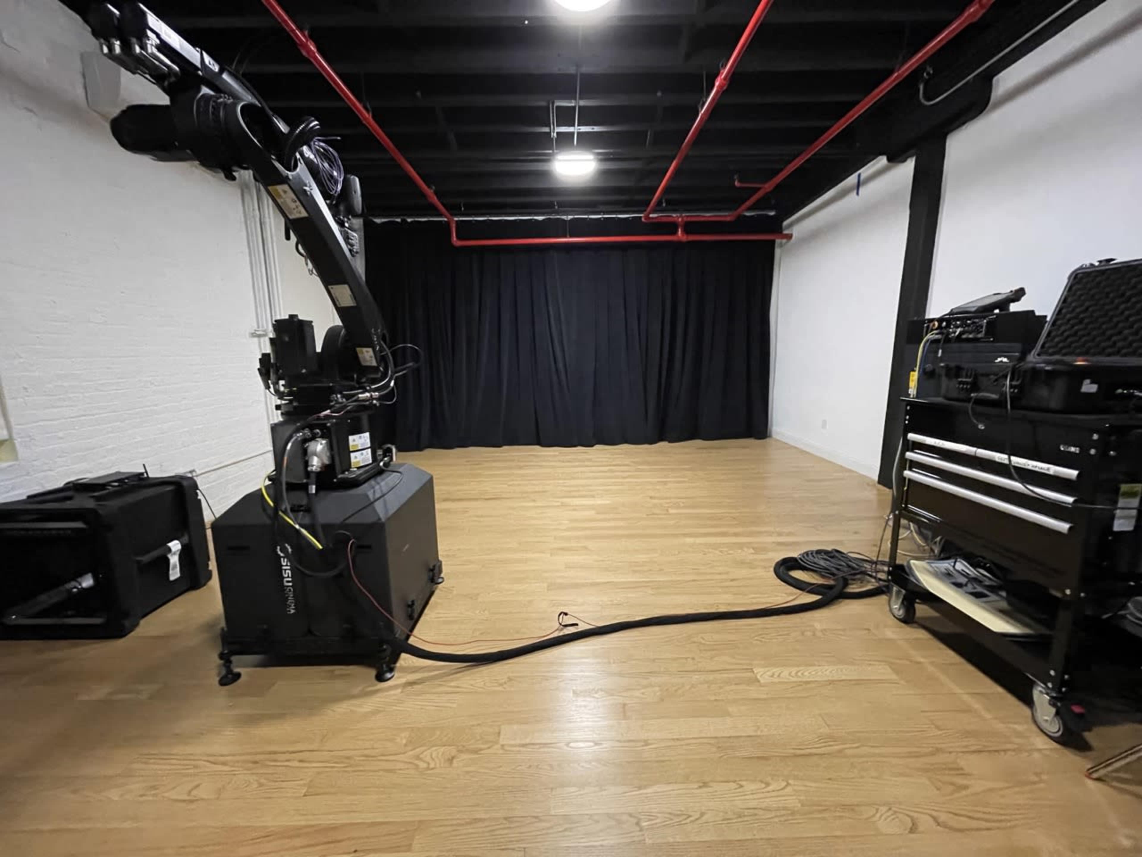 A spacious studio with wooden flooring, a black curtain backdrop, and a camera on a movable rig positioned to the left.