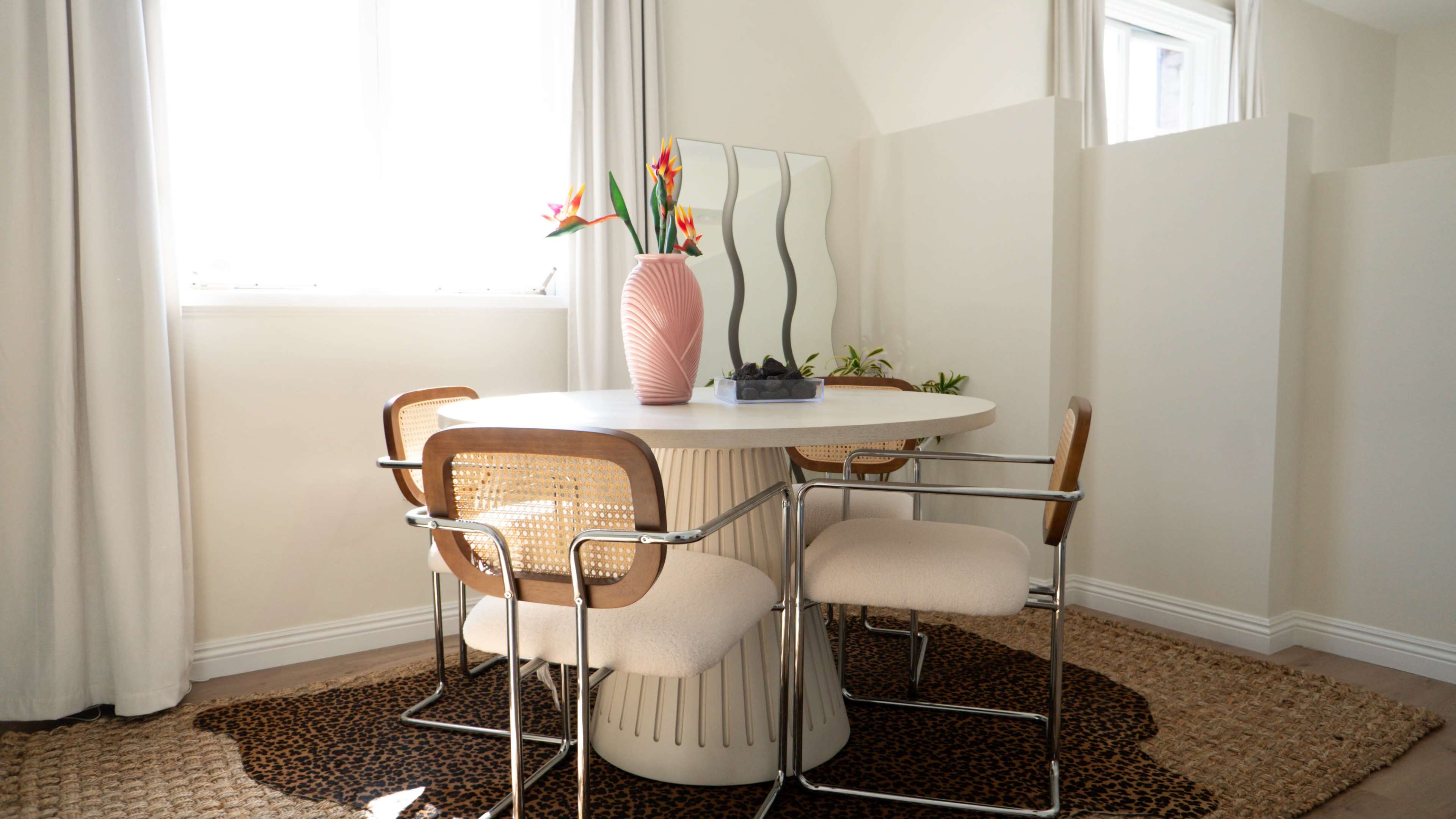 A modern dining area features a round table with a pedestal base, surrounded by four chairs, and adorned with a tall vase of flowers.