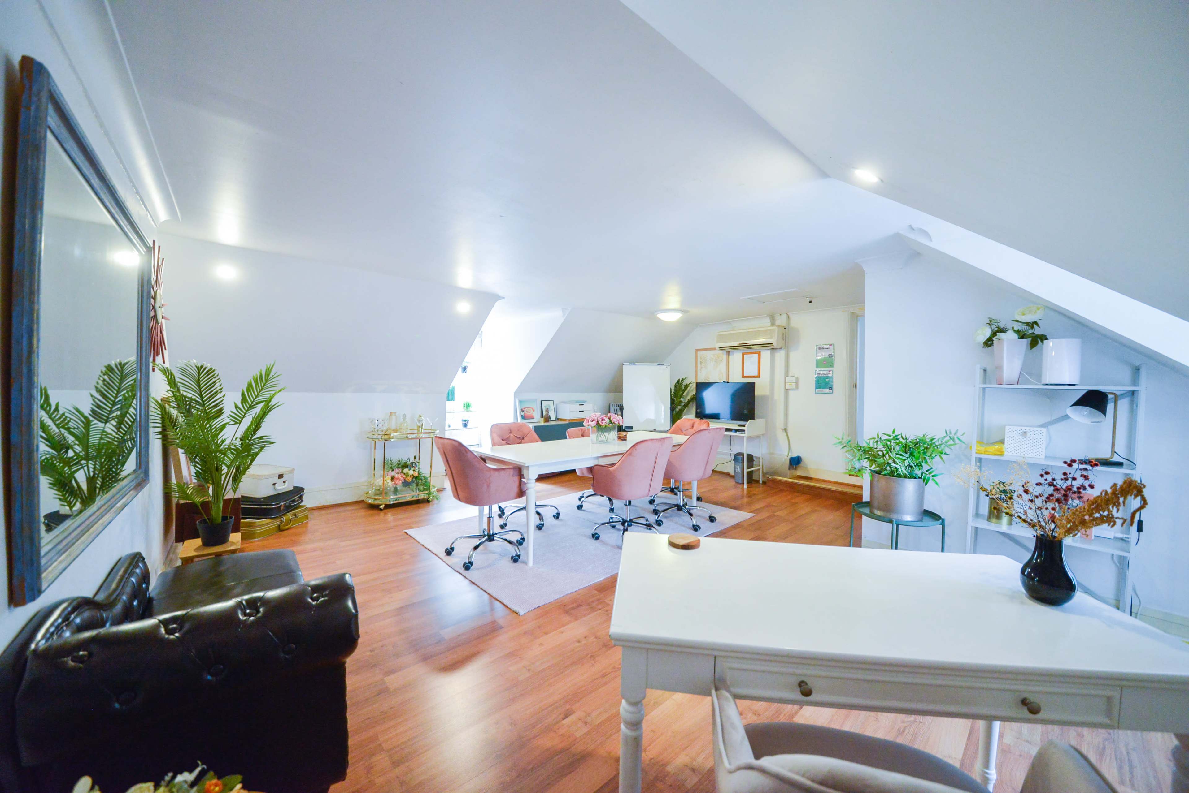 A well-lit, modern office space with a large window, featuring several pink chairs around a white table and minimalistic decor elements.