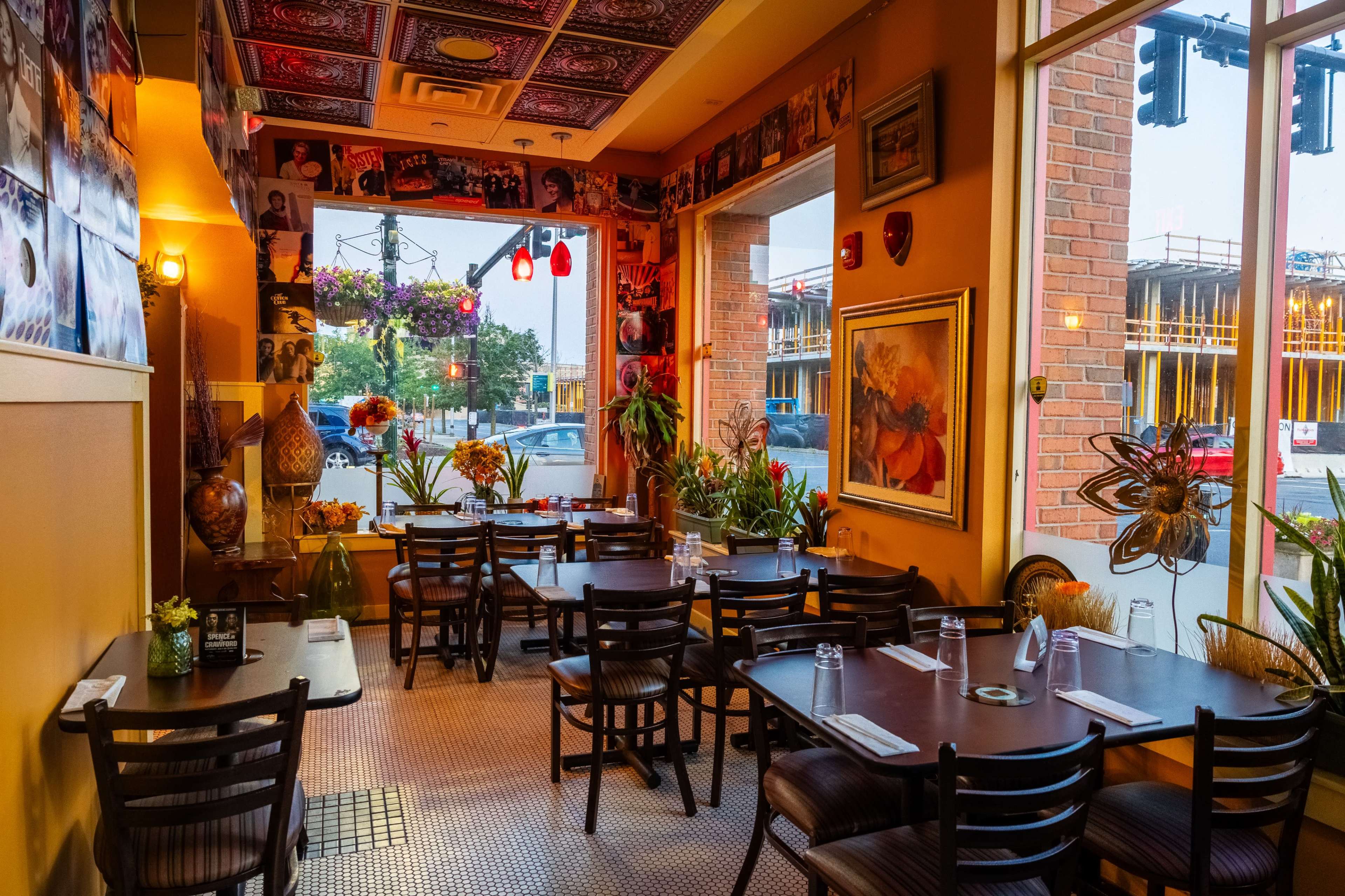 The interior of a restaurant with tables set for dining, decorated with plants and colorful wall art.