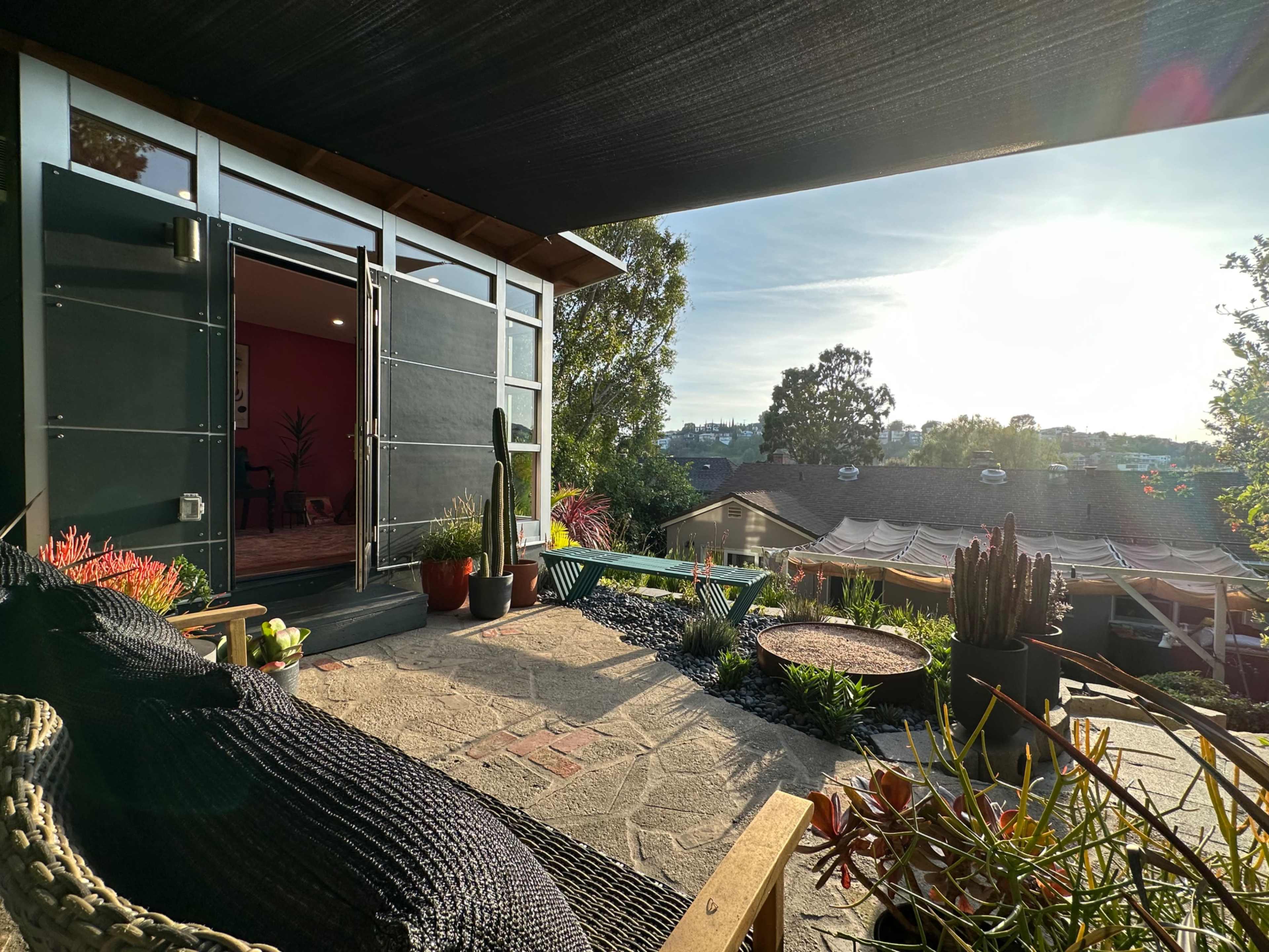 A patio with a view of a landscape, featuring plants and modern furniture, along with an open door leading into a room.