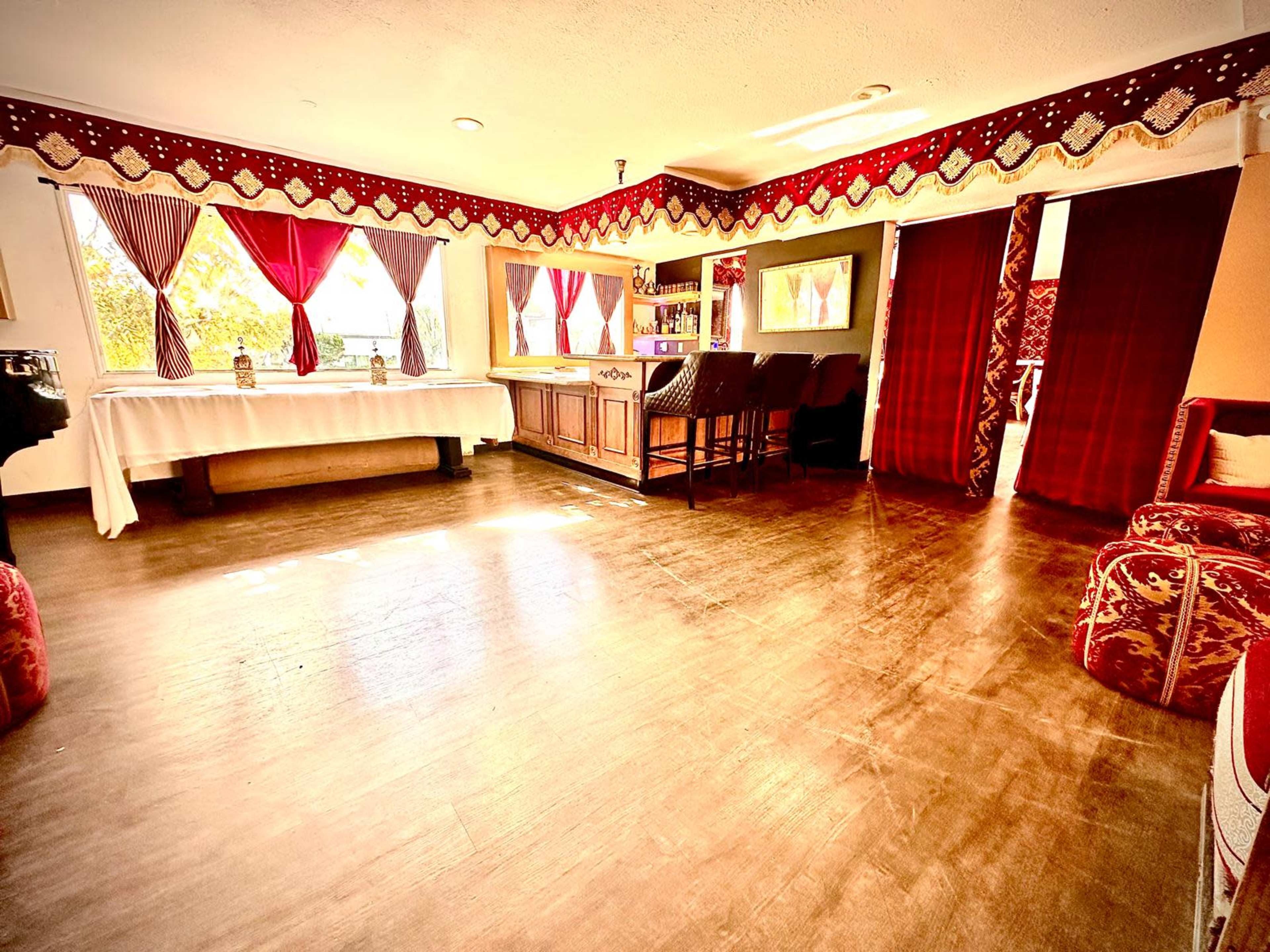 The image shows an interior room featuring a bar area, wooden flooring, and decorative curtains with a red and patterned design.