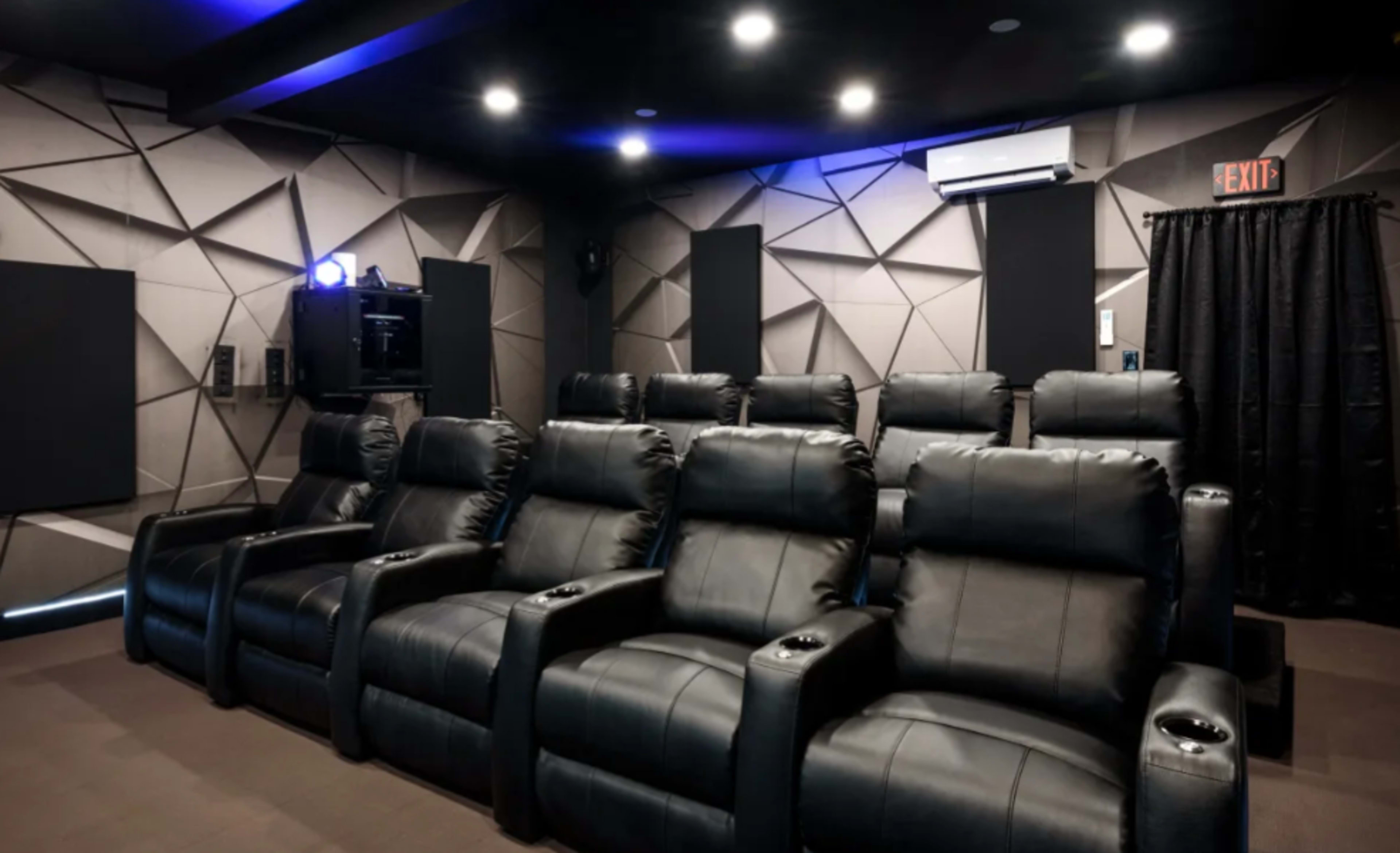 A home theater room featuring several black reclining chairs arranged in a rows, with a geometric wall design and ambient lighting.