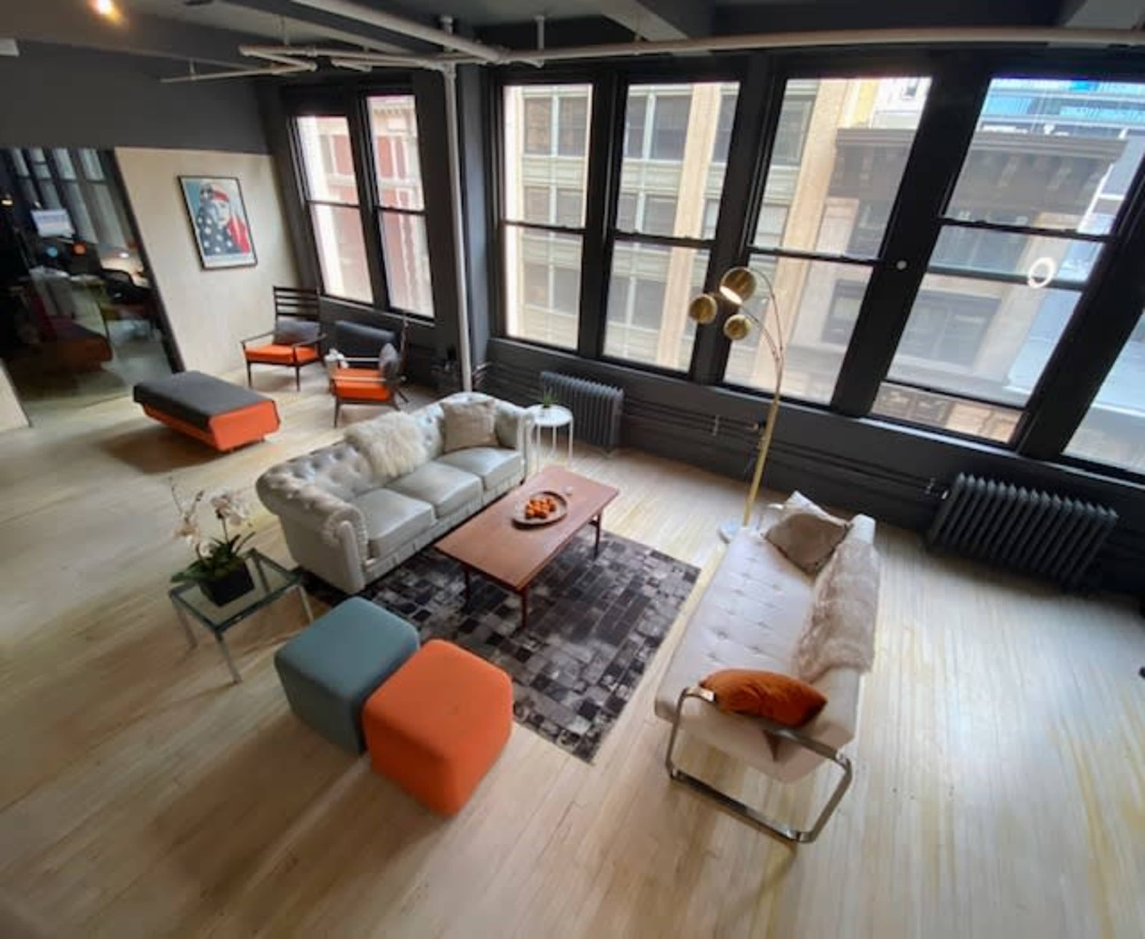 A modern living space featuring a sofa, a coffee table, colorful ottomans, and large windows allowing natural light to enter.