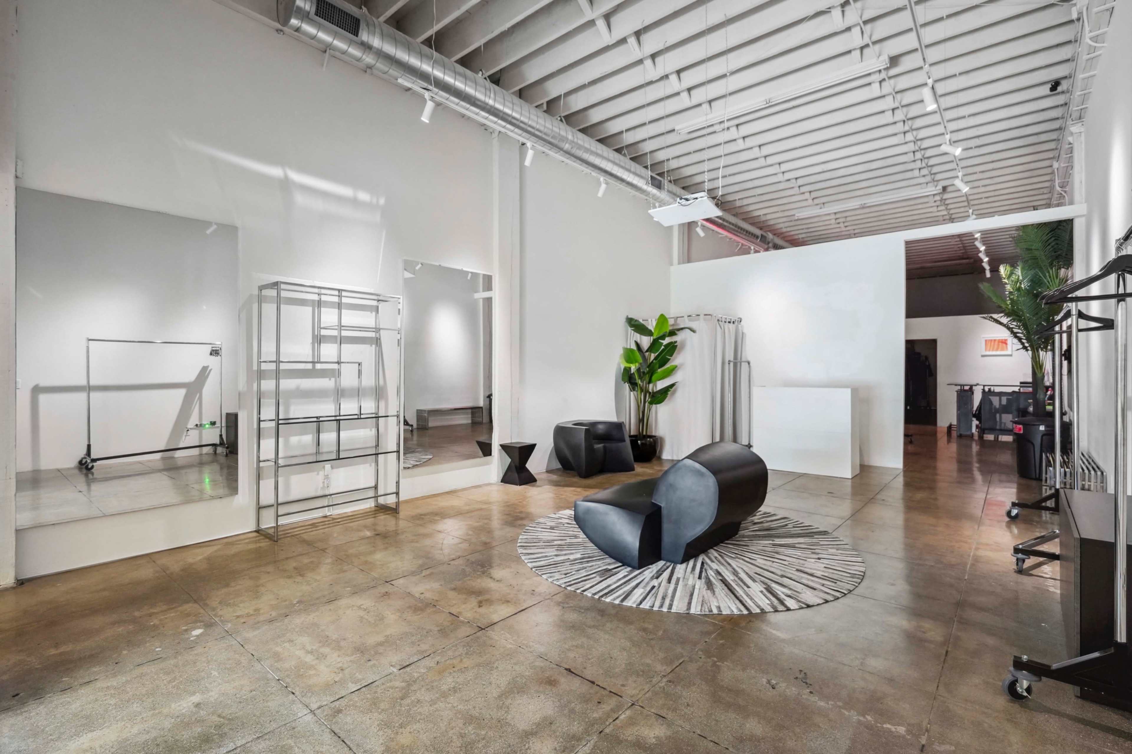 A spacious interior with polished concrete floors, large mirrors, a black curved sofa, a round rug, a tall potted plant, and minimalist shelving units.