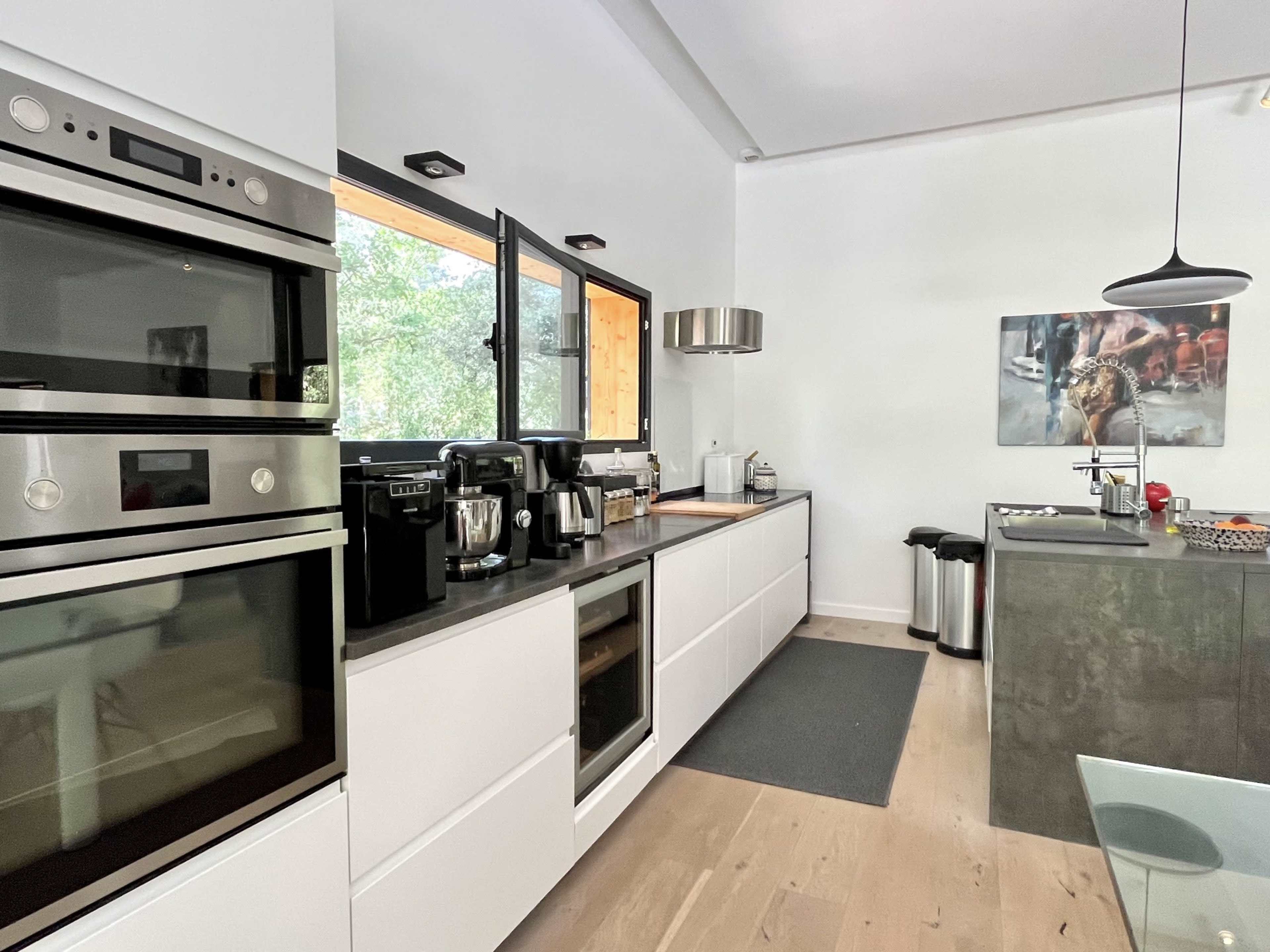 The kitchen features modern appliances, including built-in ovens and coffee makers, with a minimalist design and ample natural light from a window.
