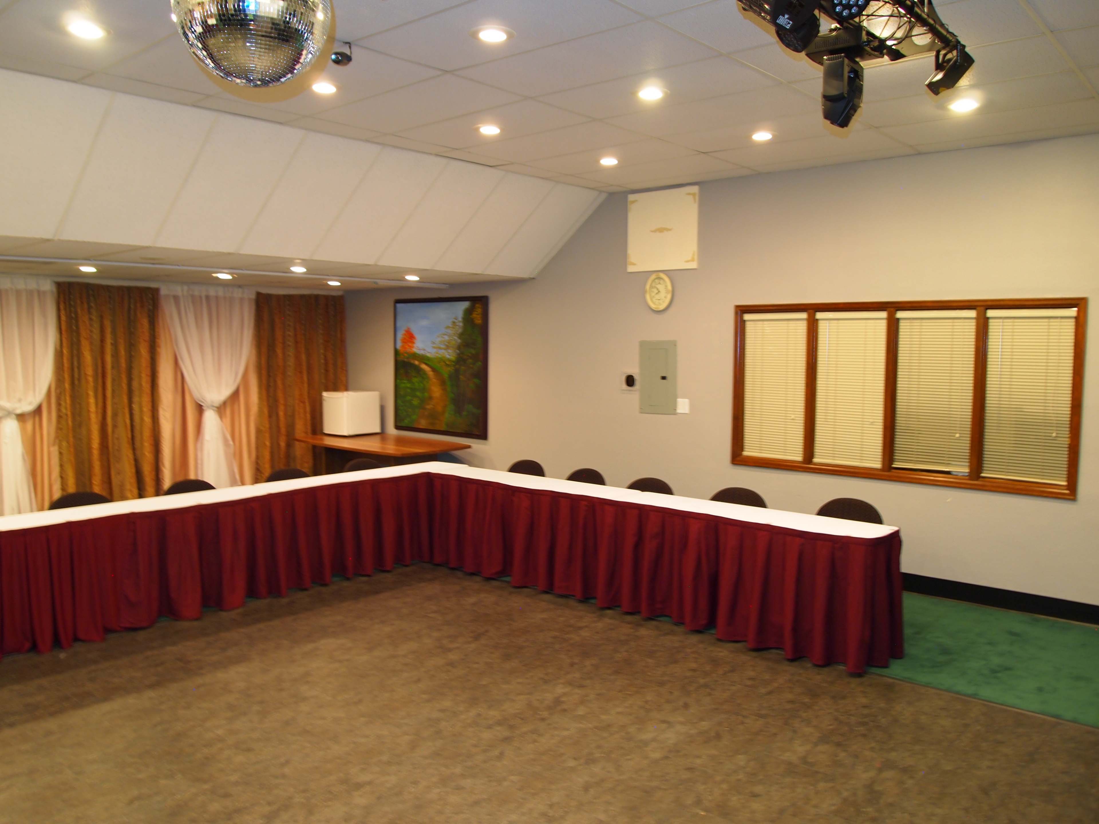 A conference room features a long table surrounded by chairs, with a disco ball hanging from the ceiling and a painting on the wall.