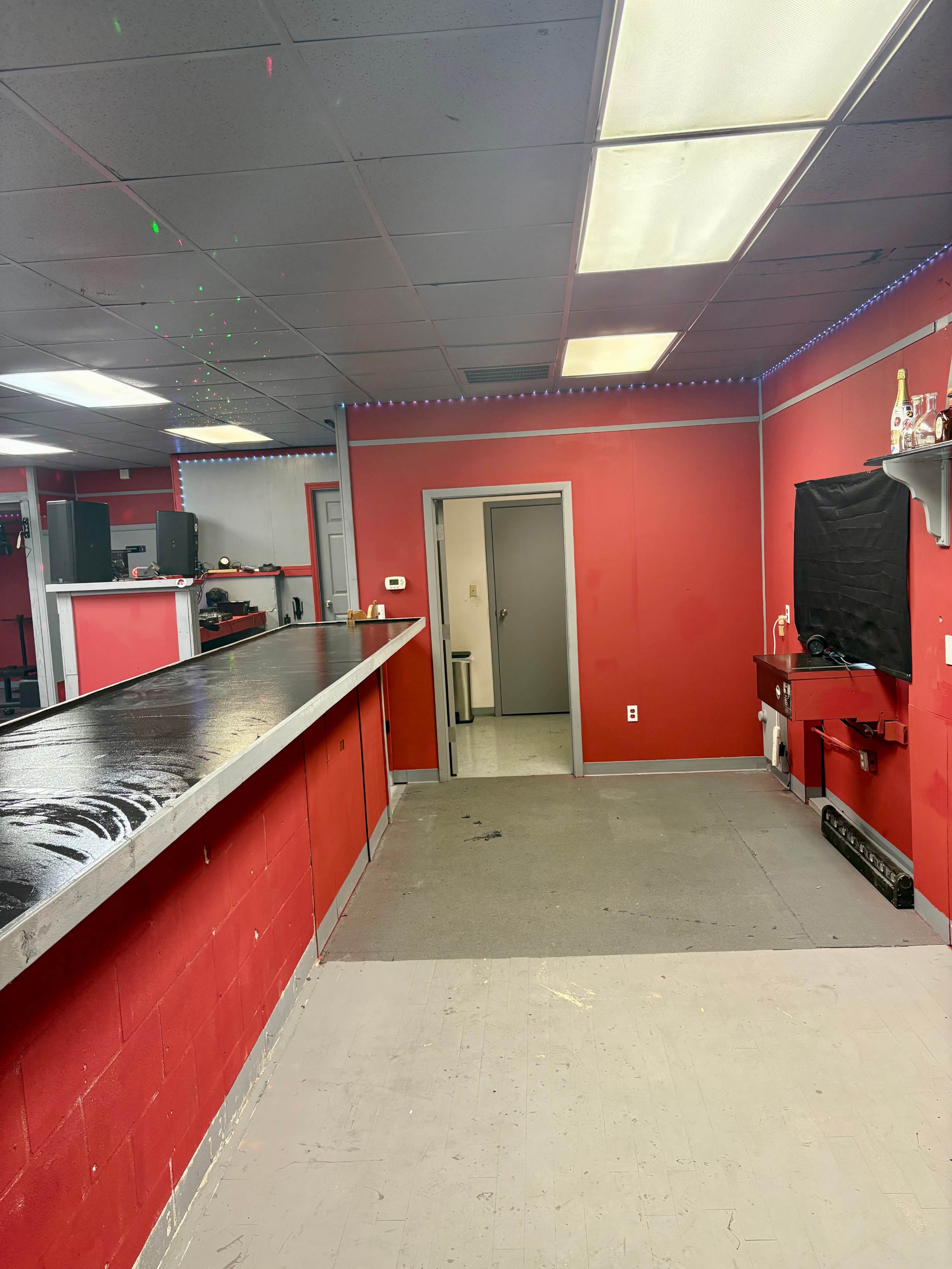 The image shows a red-walled room with a long black counter, gray flooring, and a doorway leading to another room at the back.