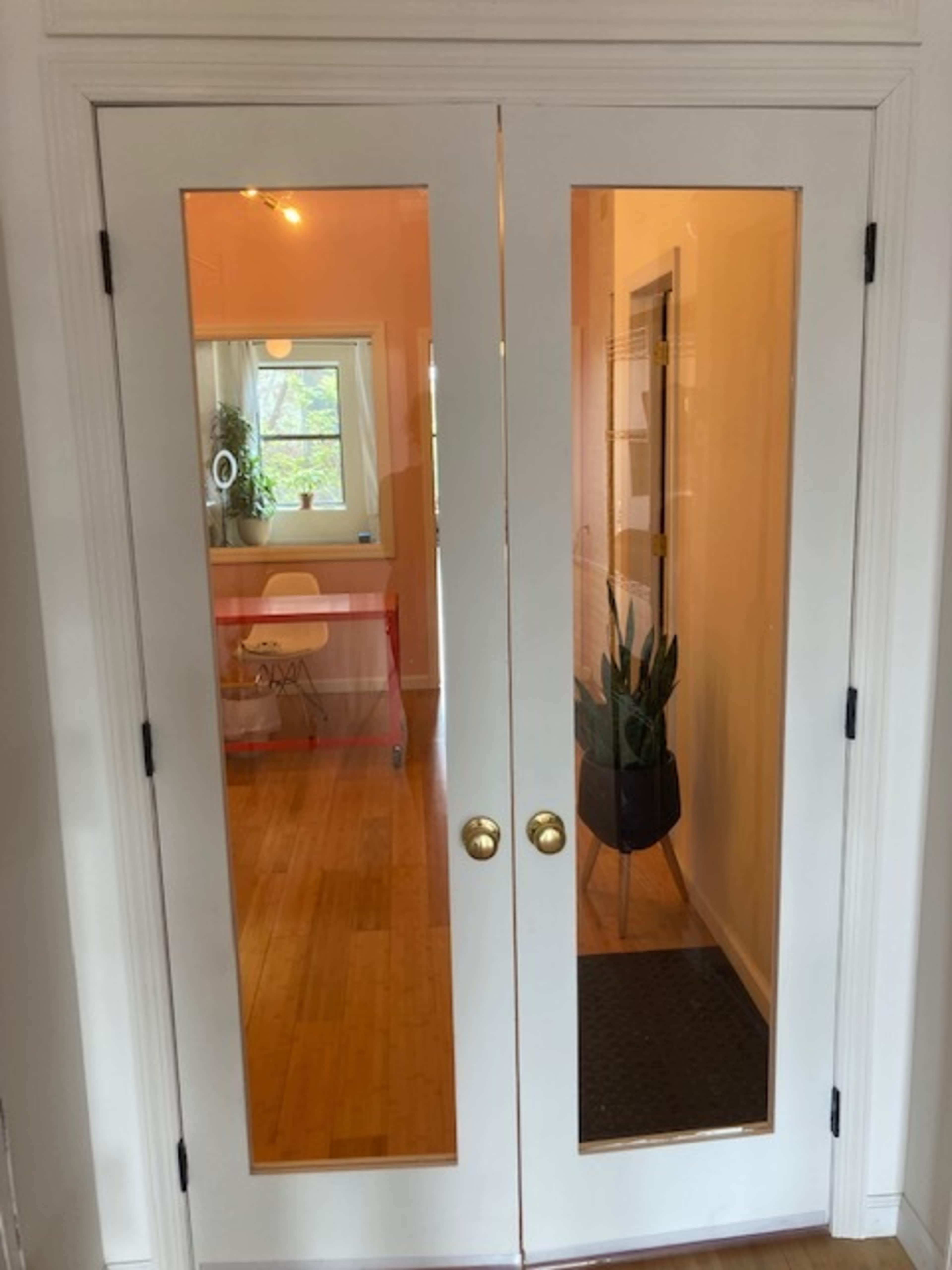 A pair of white double doors with glass panes, leading into a room with light-colored walls and a small table visible inside.