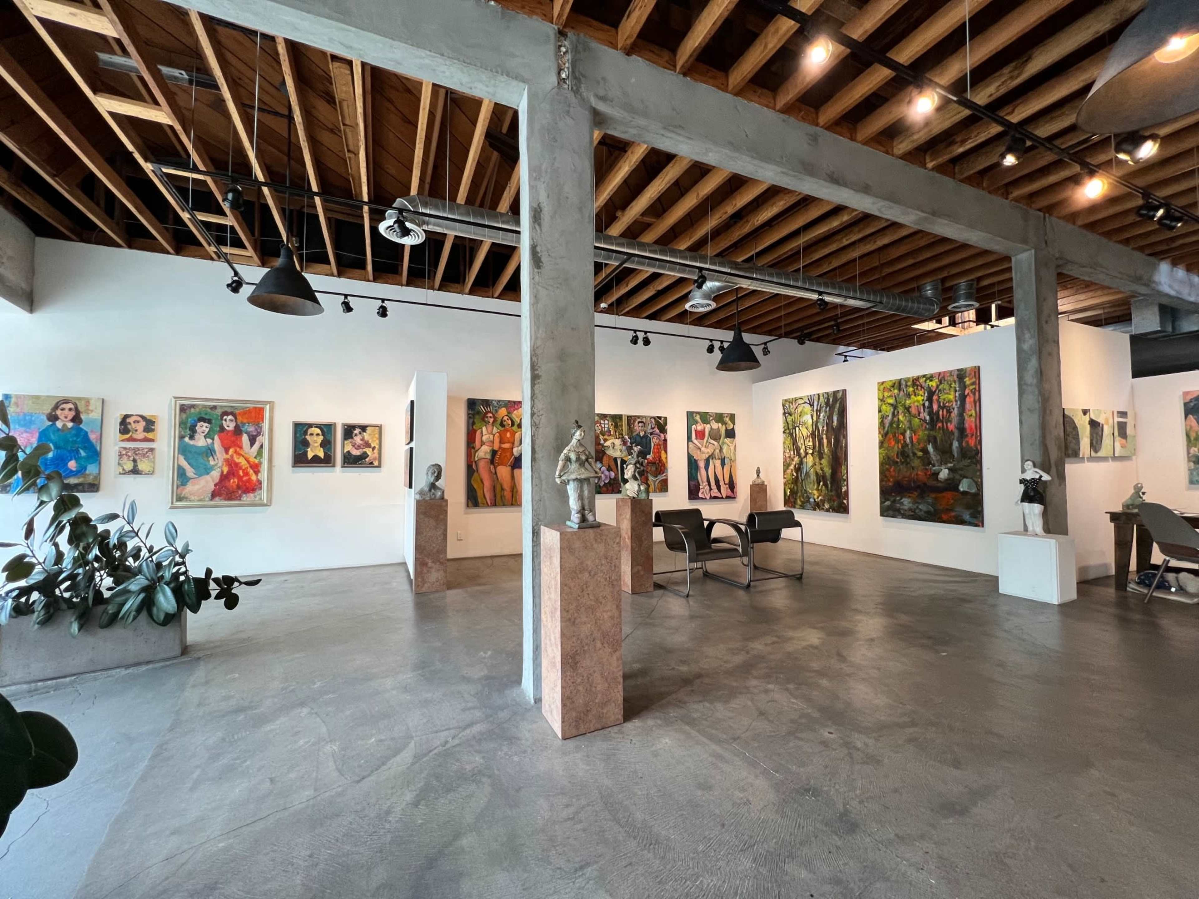 An art gallery featuring various paintings on the walls, sculptures in the center, and open space with a polished concrete floor.