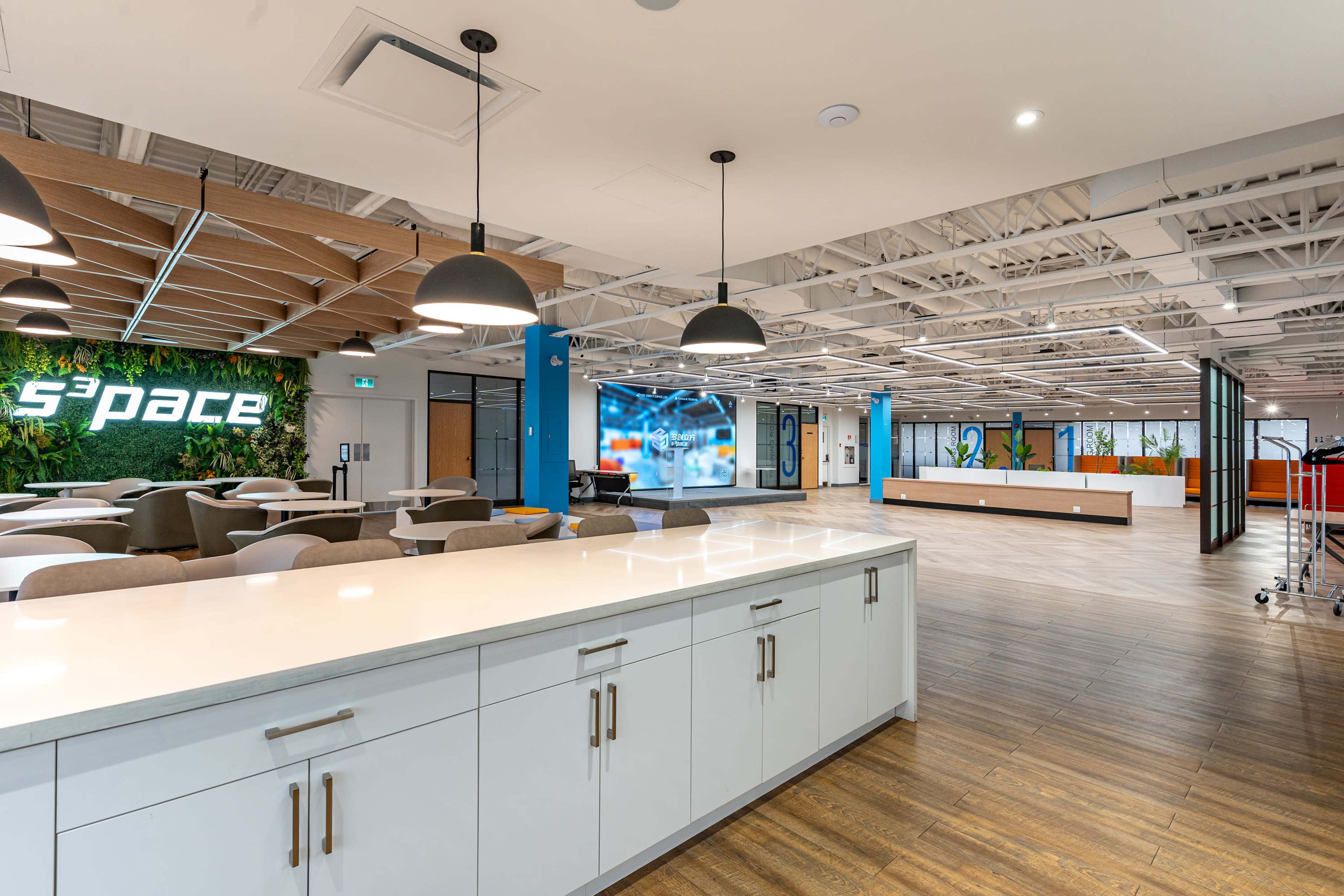 A modern office space featuring a white countertop, seating areas, and vibrant wall decorations, including a logo and digital displays.