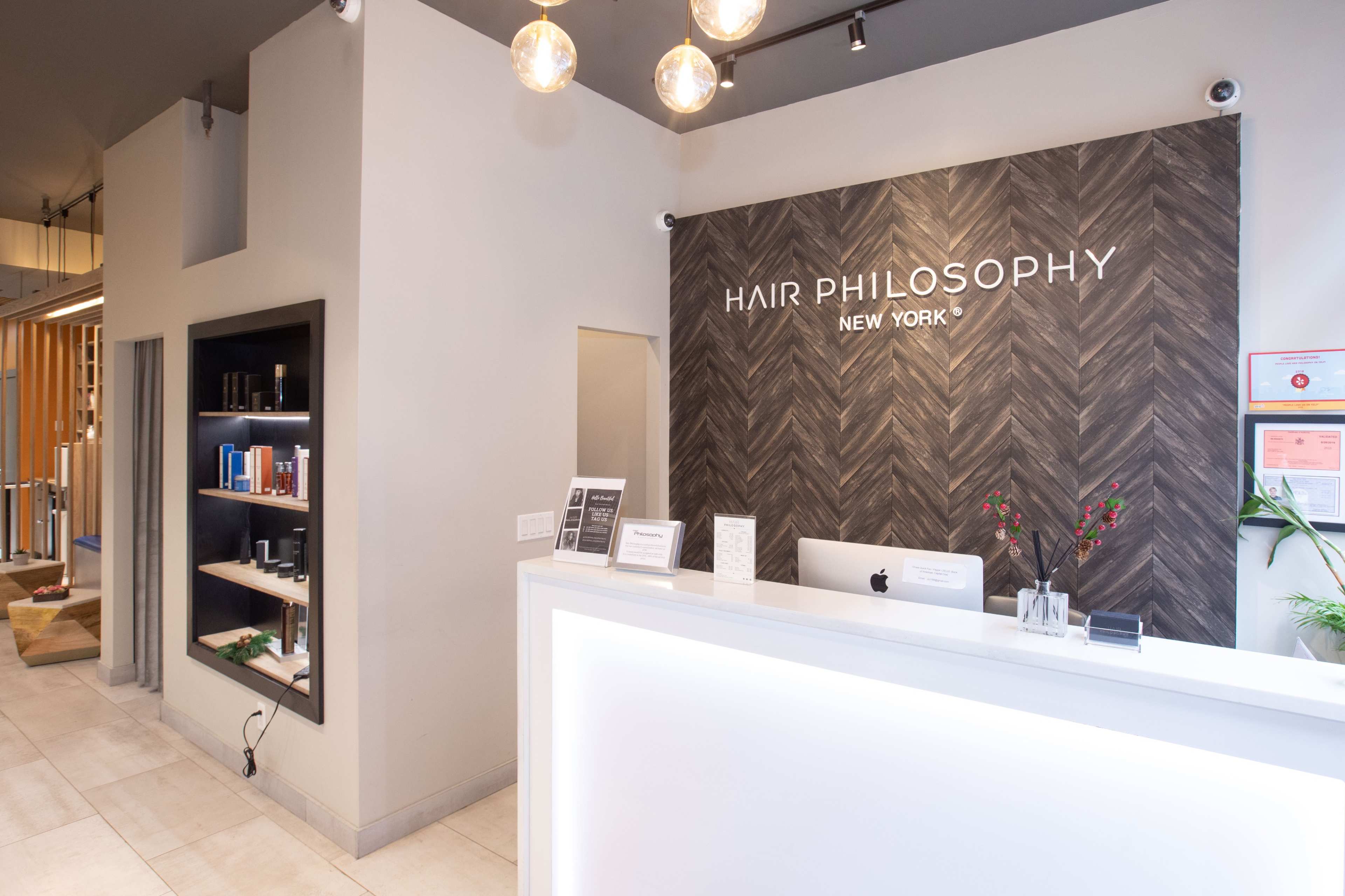 The reception area of a hair salon named "Hair Philosophy" features a sleek front desk with a modern design and products displayed on shelves.