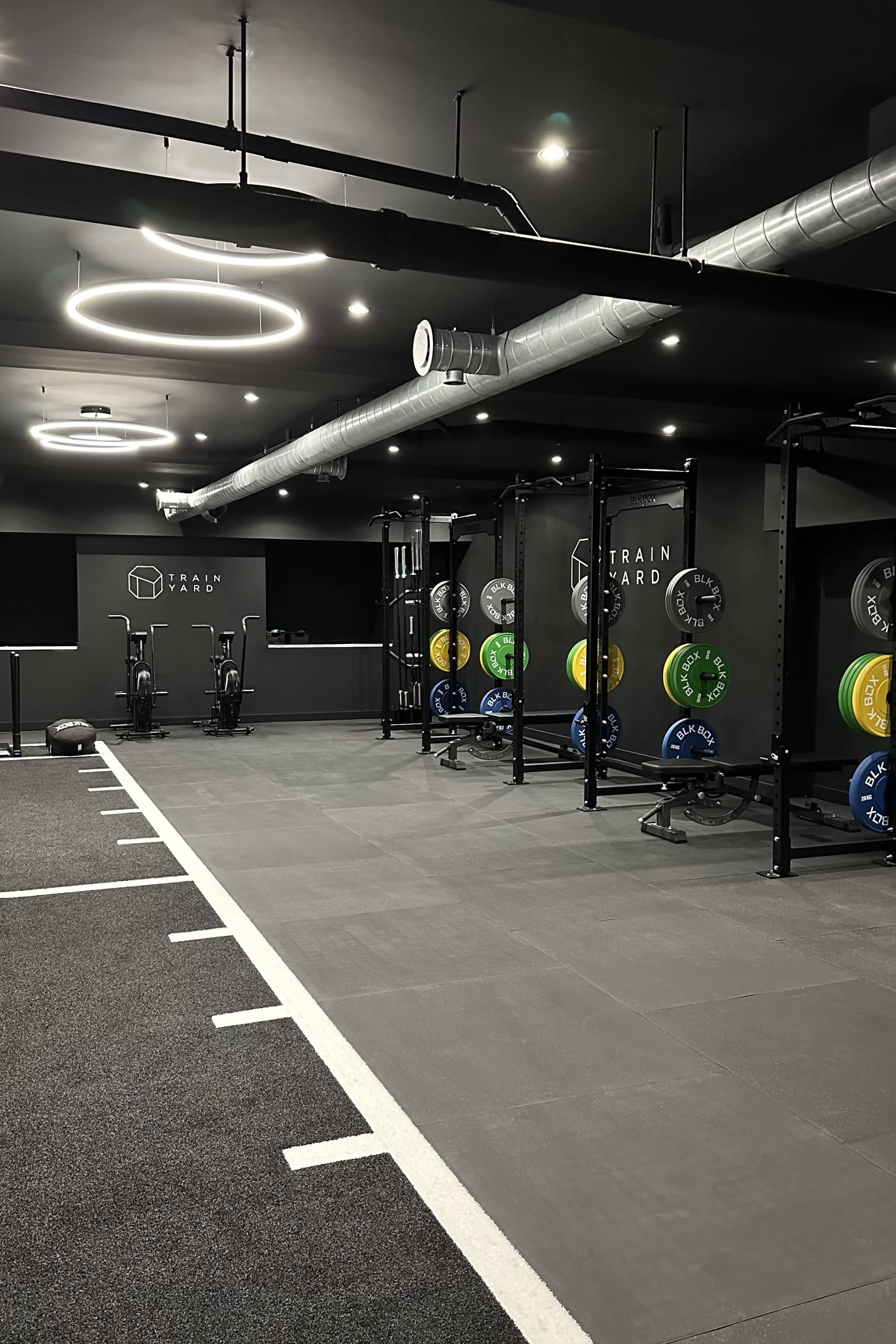 The image shows a modern gym interior with exercise equipment, weight plates, and a spacious workout area.