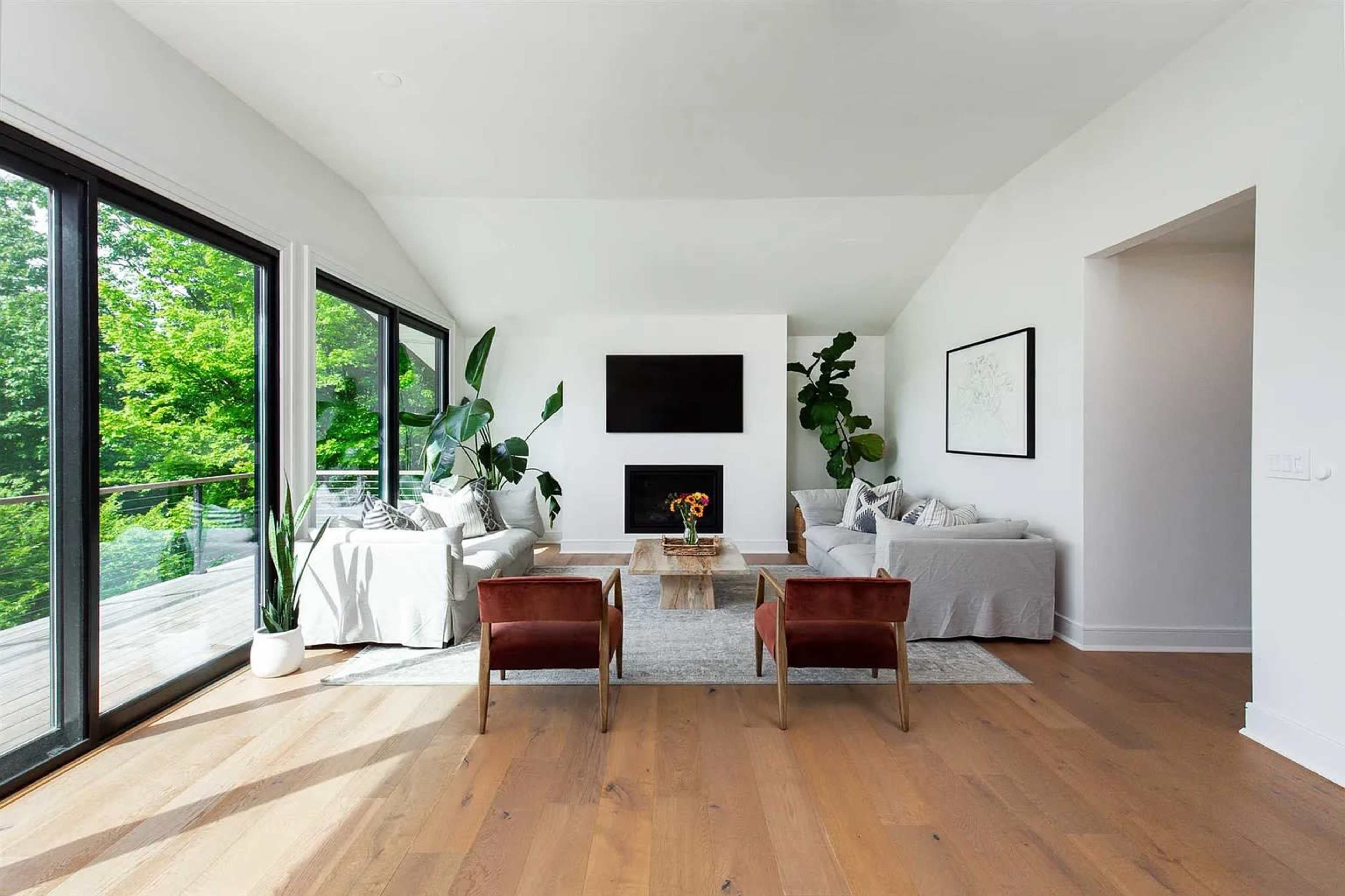 A modern living room with large windows, a fireplace, and two brown chairs facing a wooden coffee table.