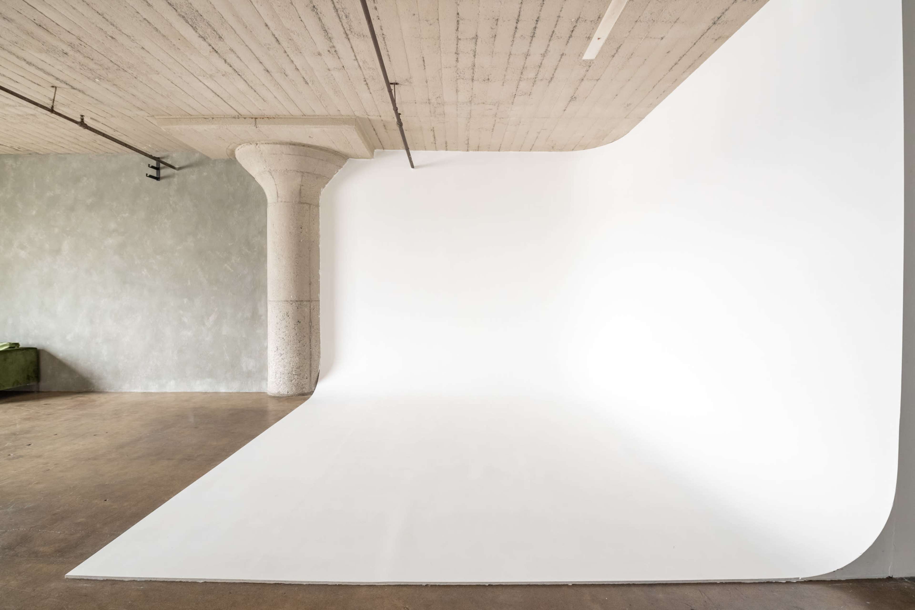 The image shows a spacious photography studio with a seamless white backdrop and a concrete column.
