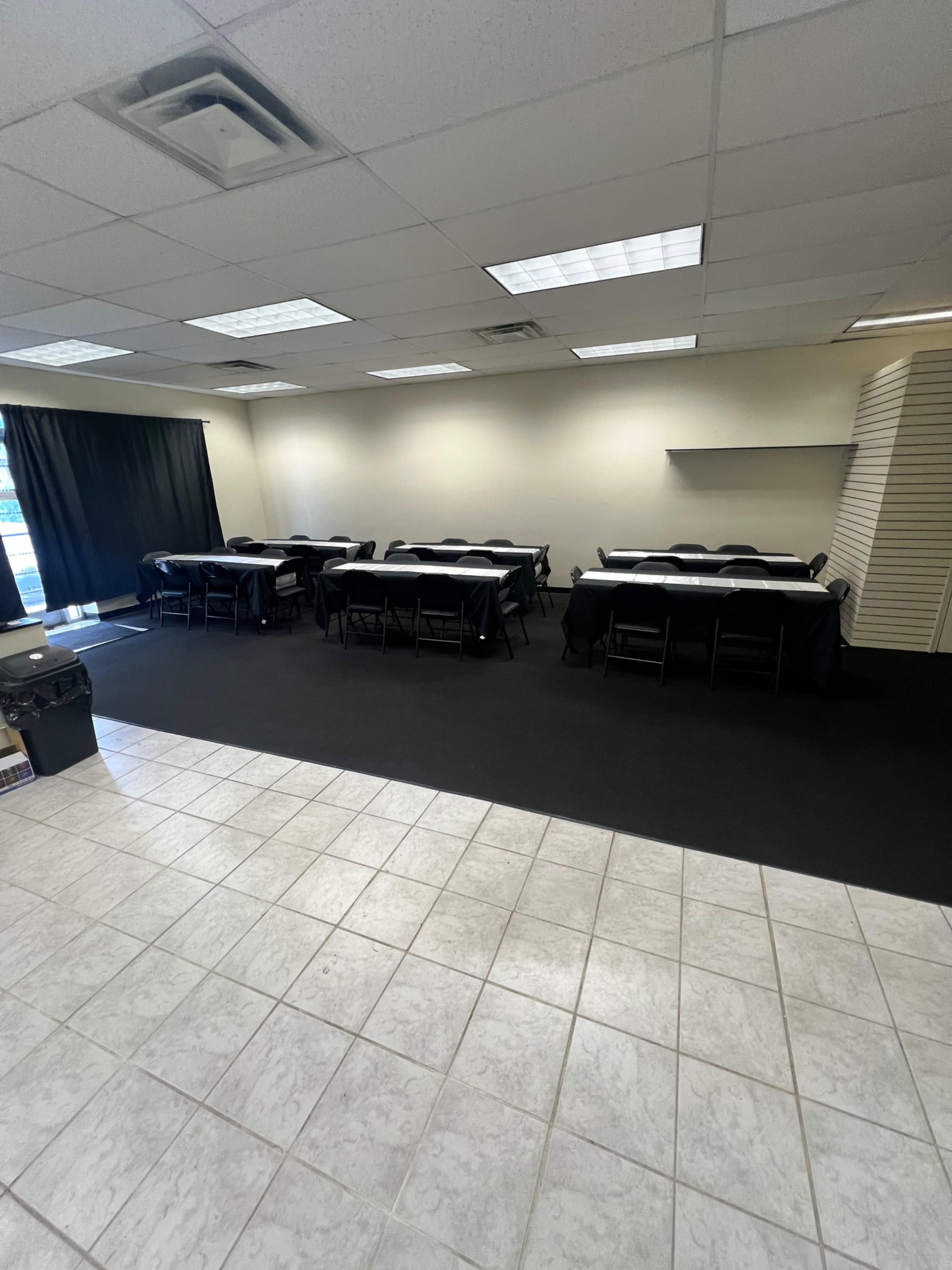 The image shows a classroom or conference room with rows of tables and chairs set up on a black carpeted floor.