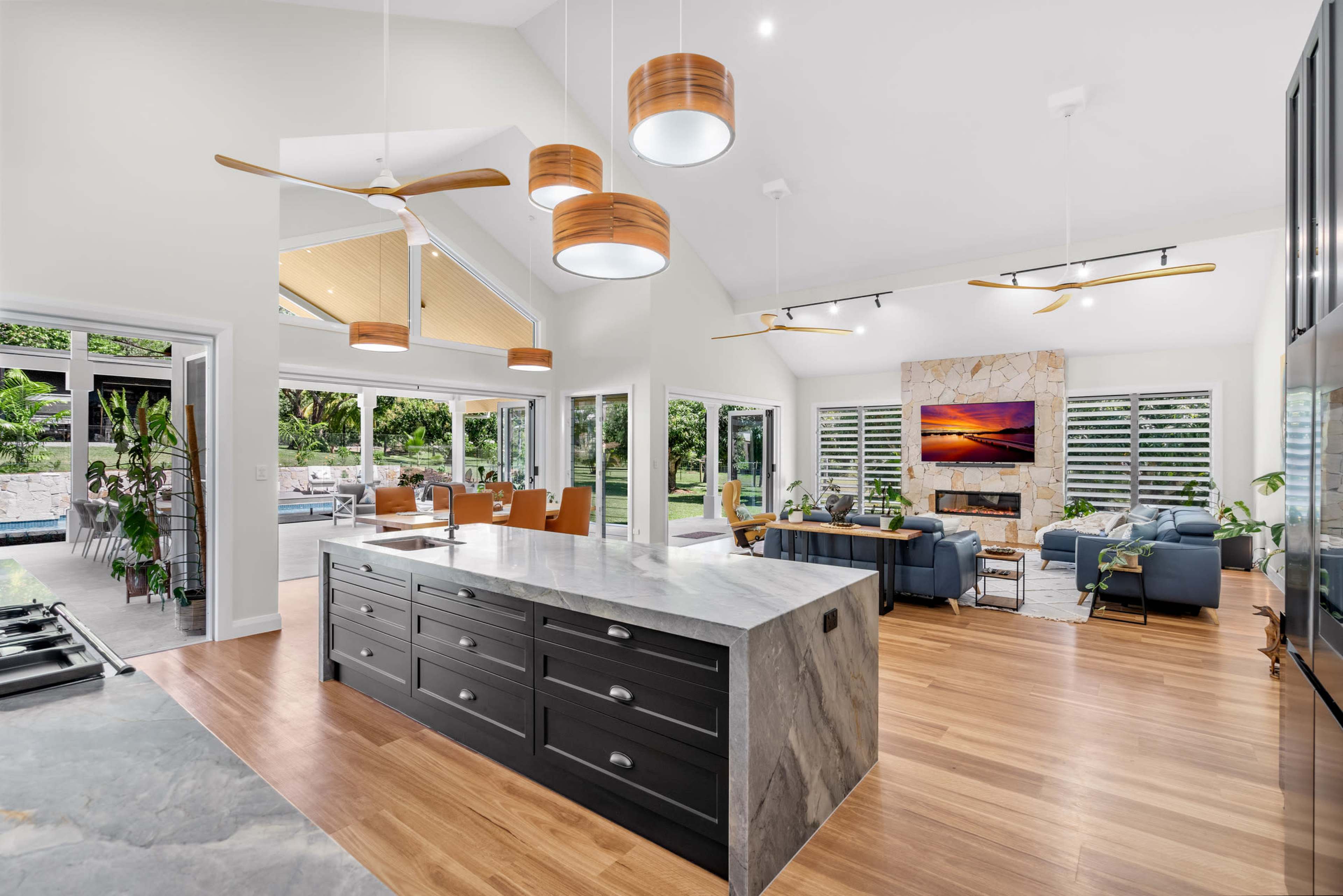 The image shows a modern open-concept living space featuring a large kitchen island, dining area, and seating area, with large windows and natural light.