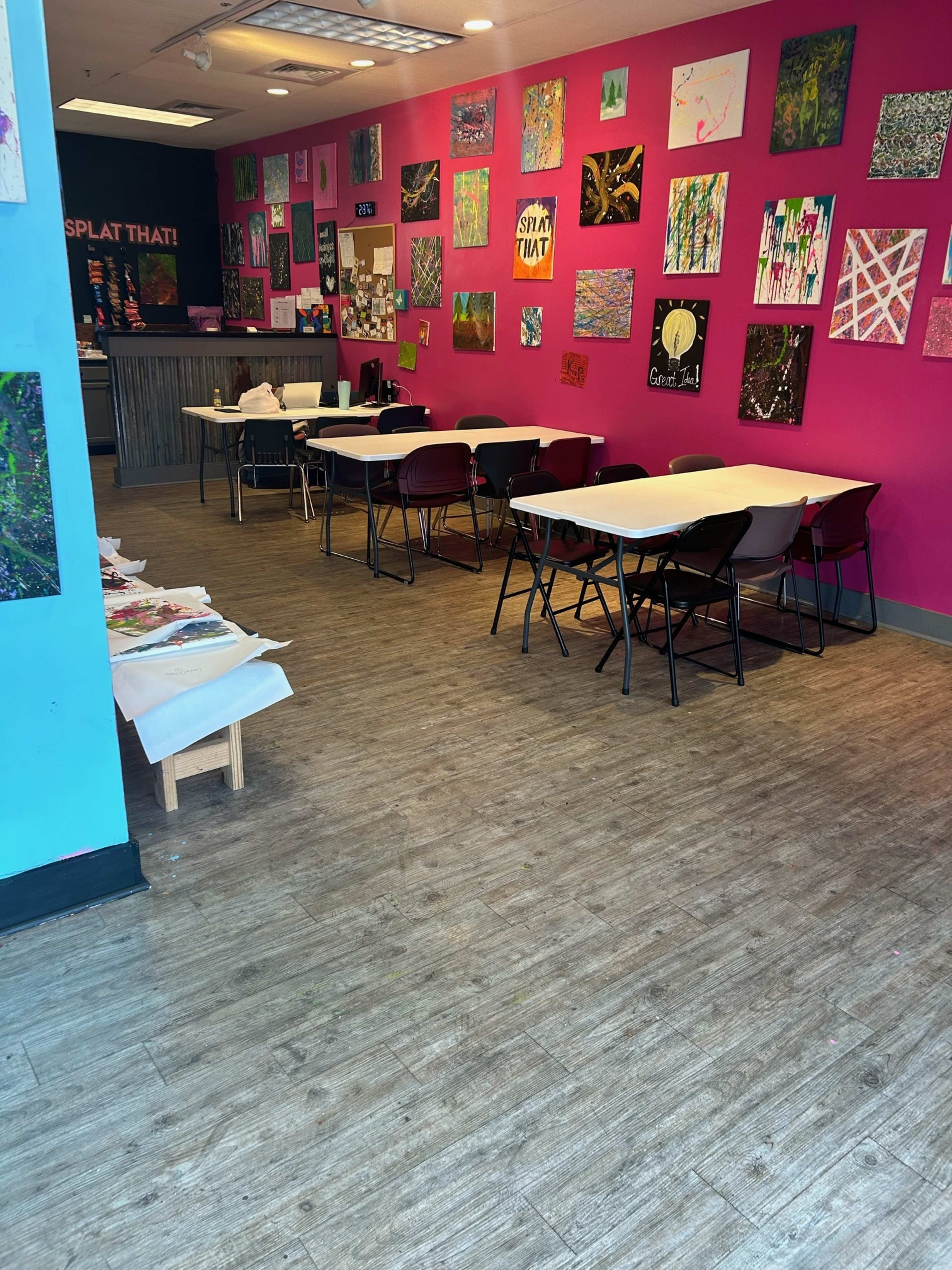 An art studio with pink walls adorned with various artworks and several tables with chairs arranged for activities.