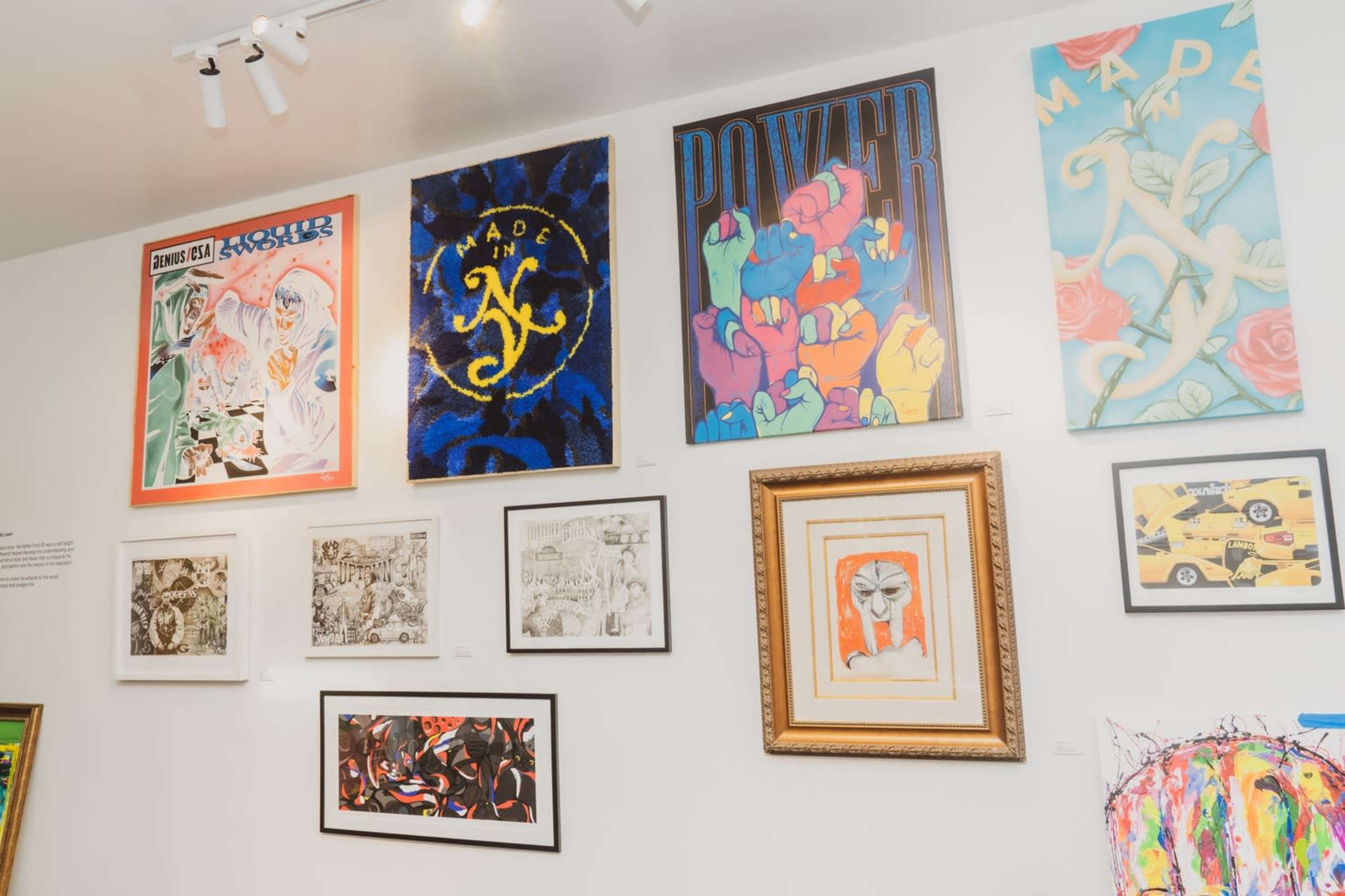 The image shows an art gallery wall with a variety of colorful paintings and framed artworks displayed in an organized manner.