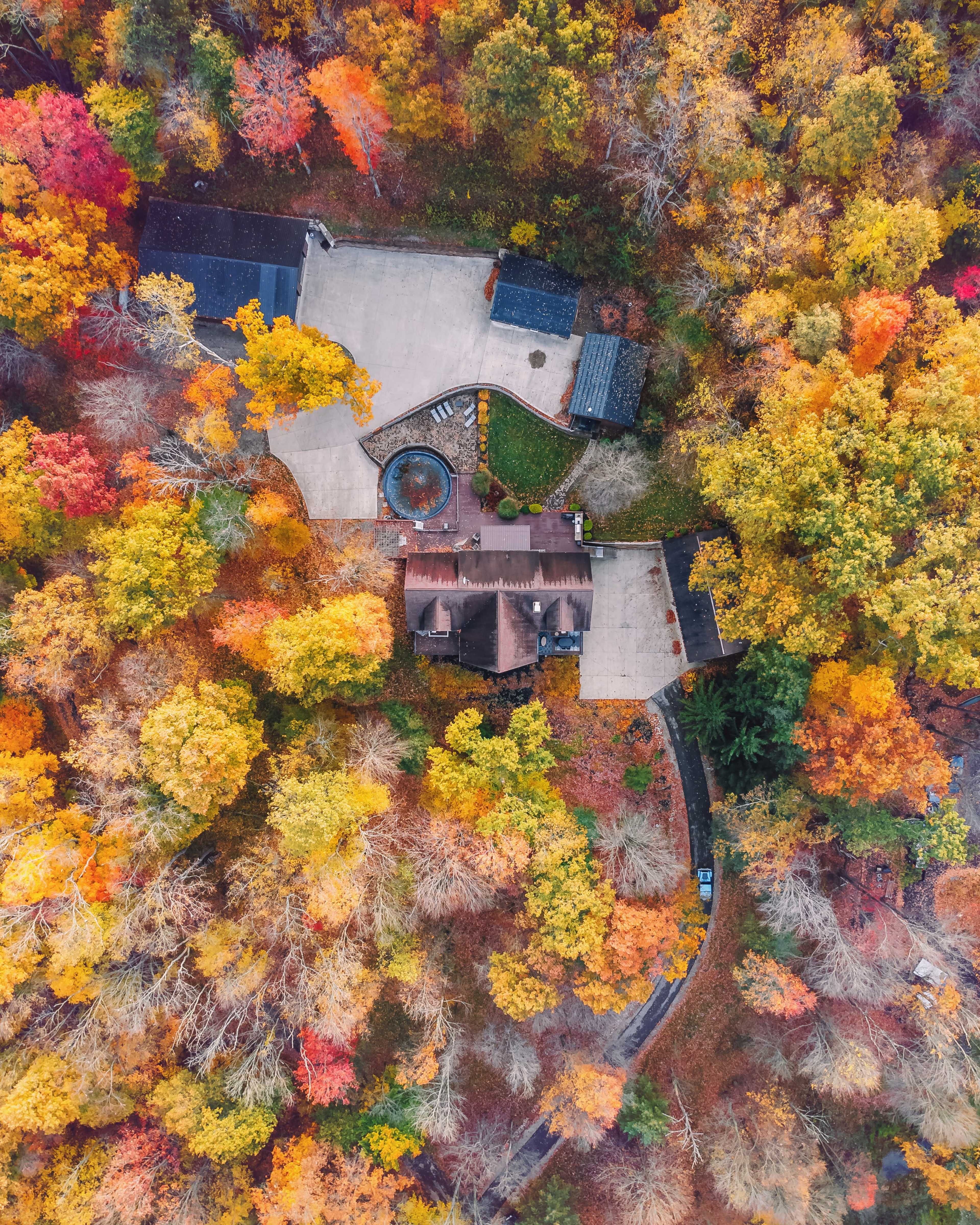 An aerial view of a house surrounded by vibrant autumn foliage in a wooded area.