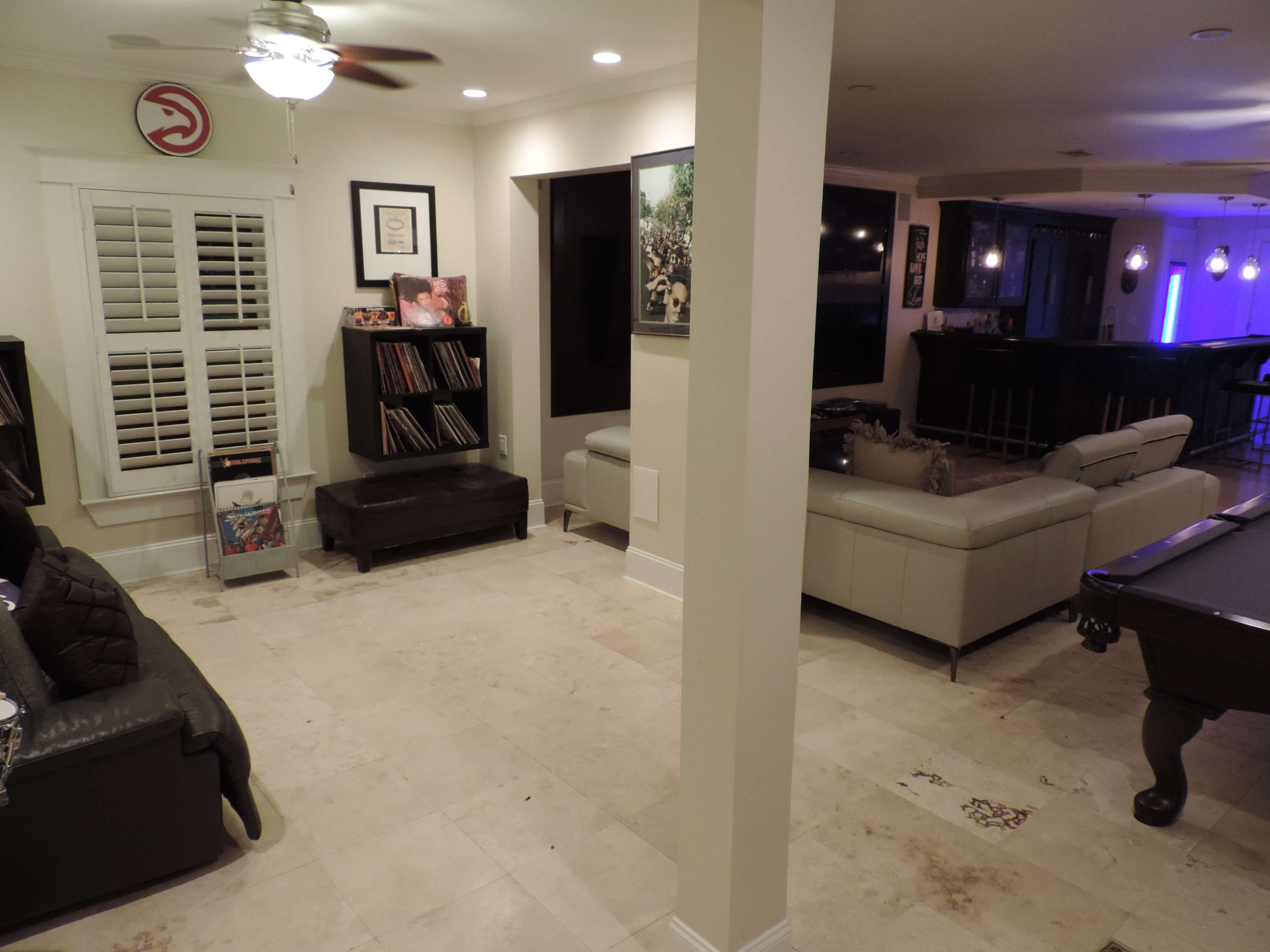 The image shows a spacious living area with a seating arrangement, a bar area in the background, and wall decorations, including framed art and a logo.