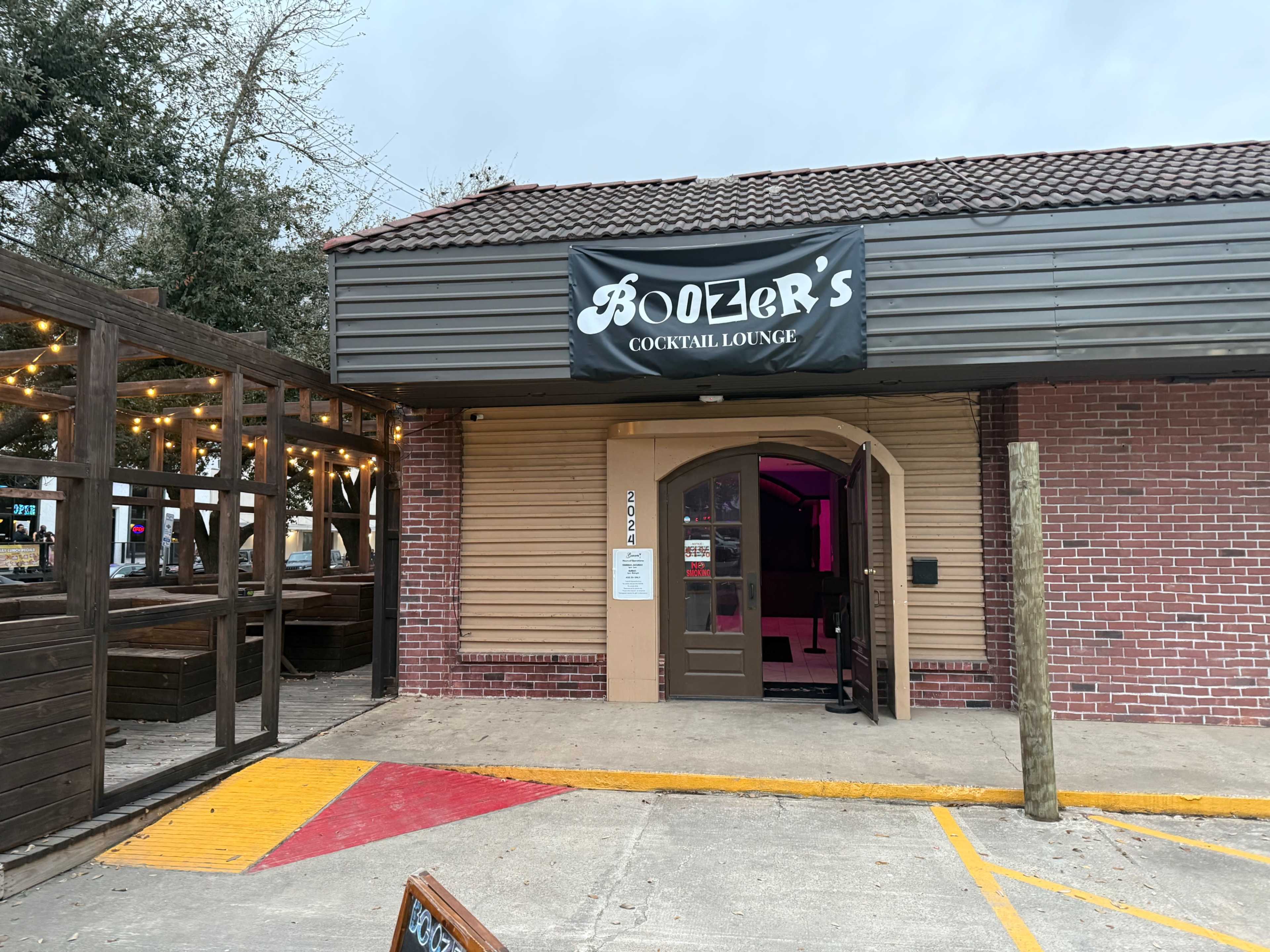 The image shows the entrance of Boozer's Cocktail Lounge, featuring a sign above the door and a outdoor seating area with string lights nearby.