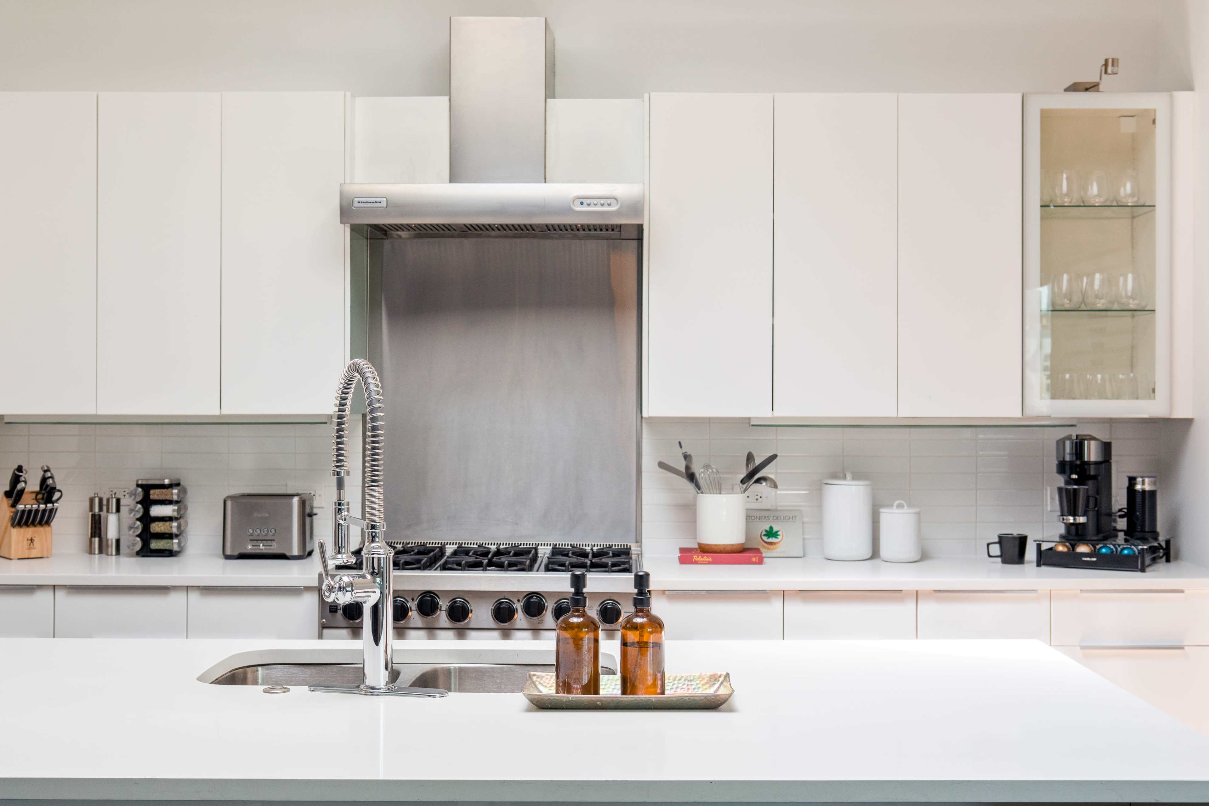 A modern kitchen features stainless steel appliances, white cabinetry, and a central island with a sink and countertop items.