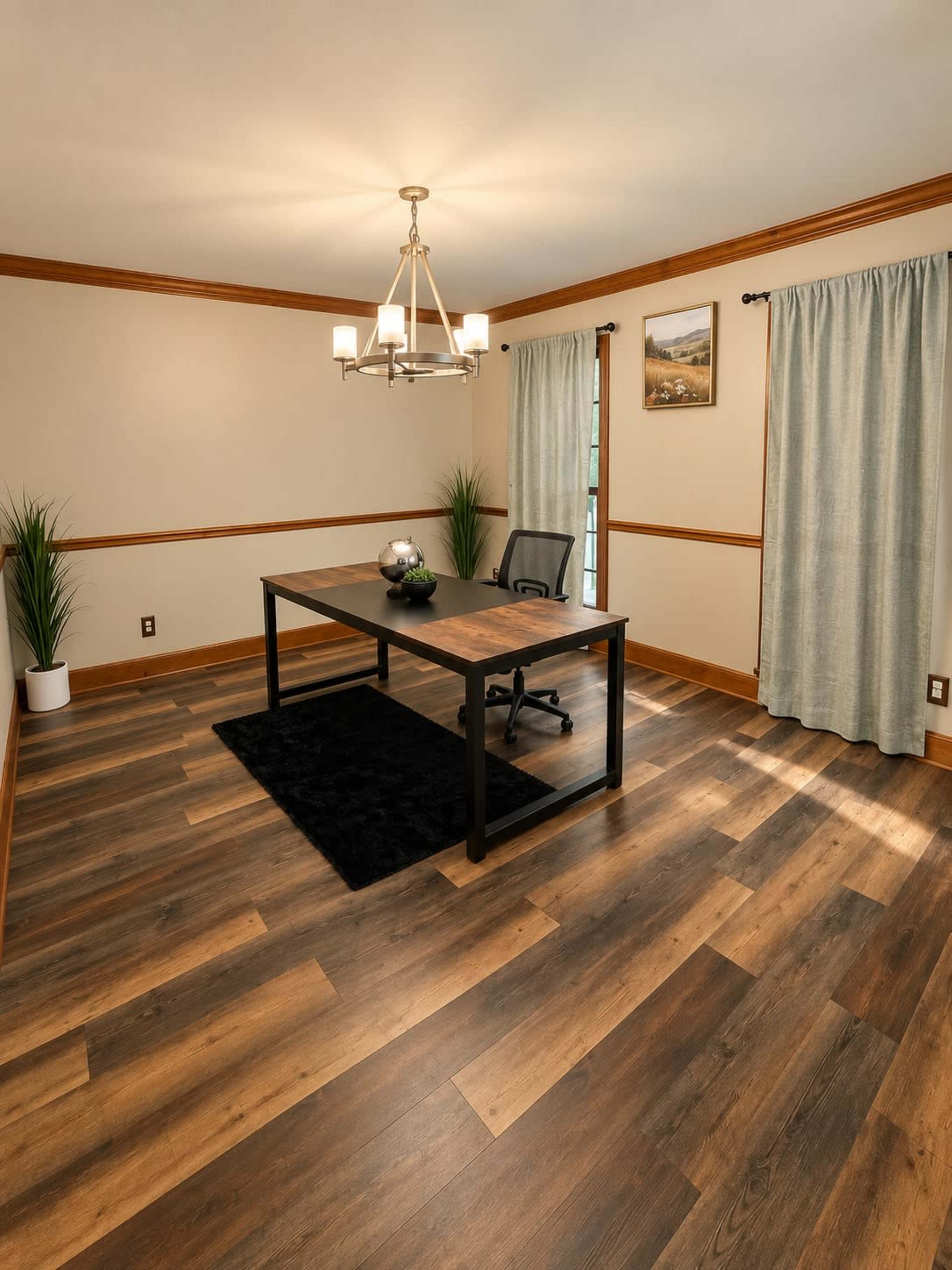 The image shows a spacious office with a large wooden table, an ergonomic chair, and decorative plants, set against light-colored walls and hardwood flooring.