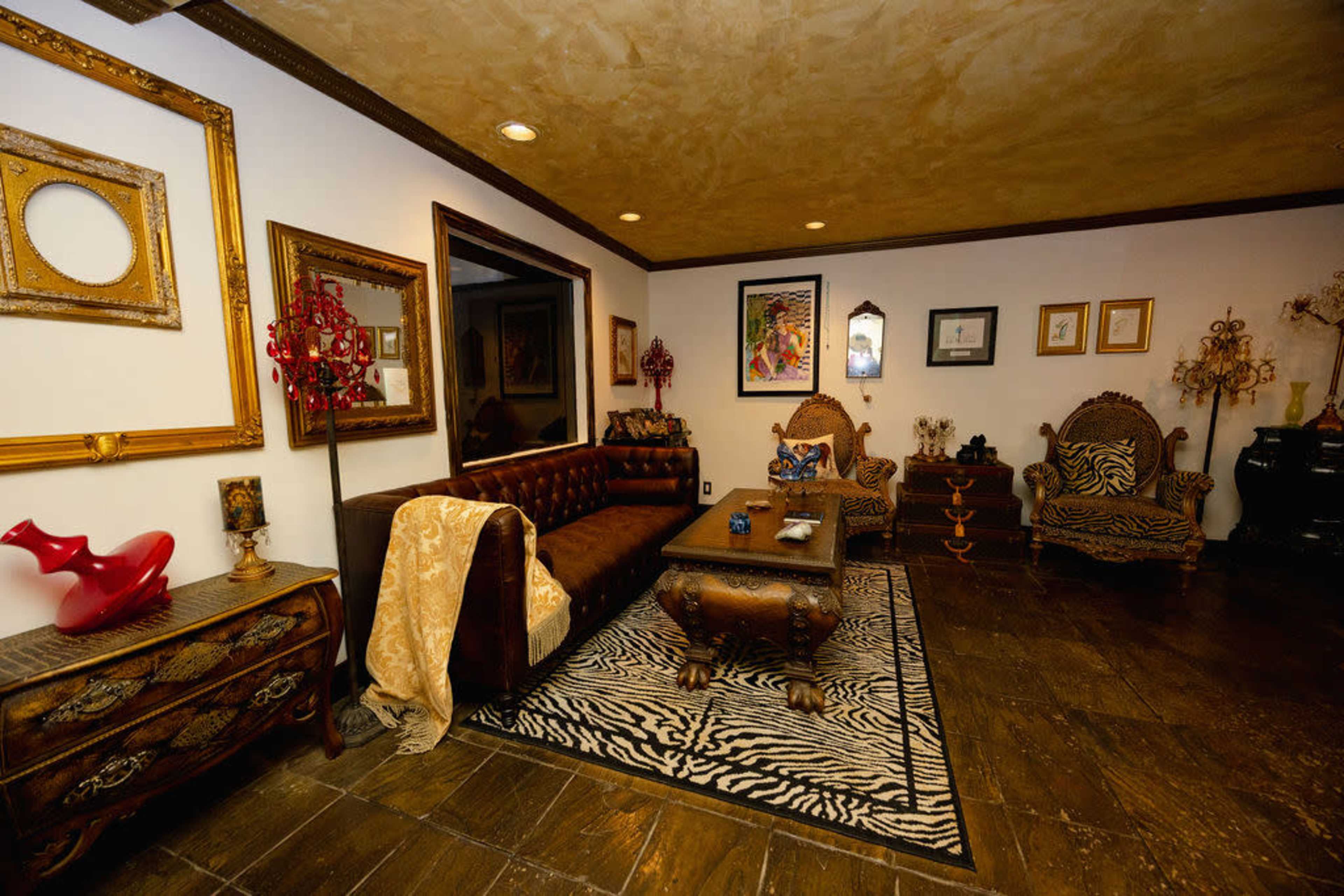 The room features ornate furniture, including a tufted brown sofa and intricately designed chairs, with decorative art and mirrors adorning the walls.