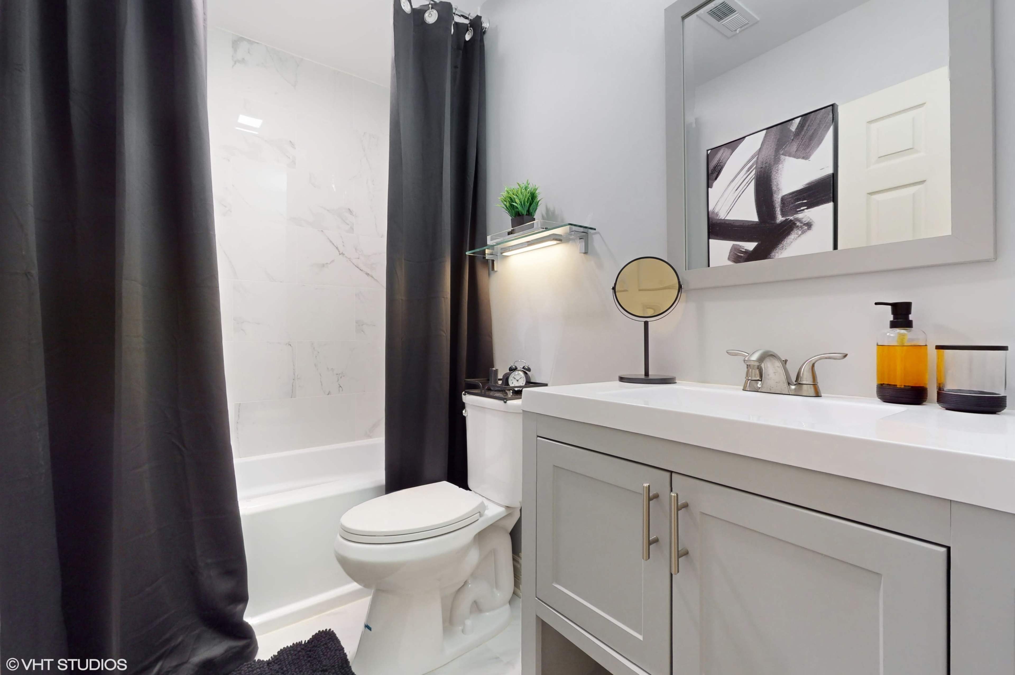 A bathroom features a tub and shower combination, a modern sink vanity, a large mirror, and dark curtains.