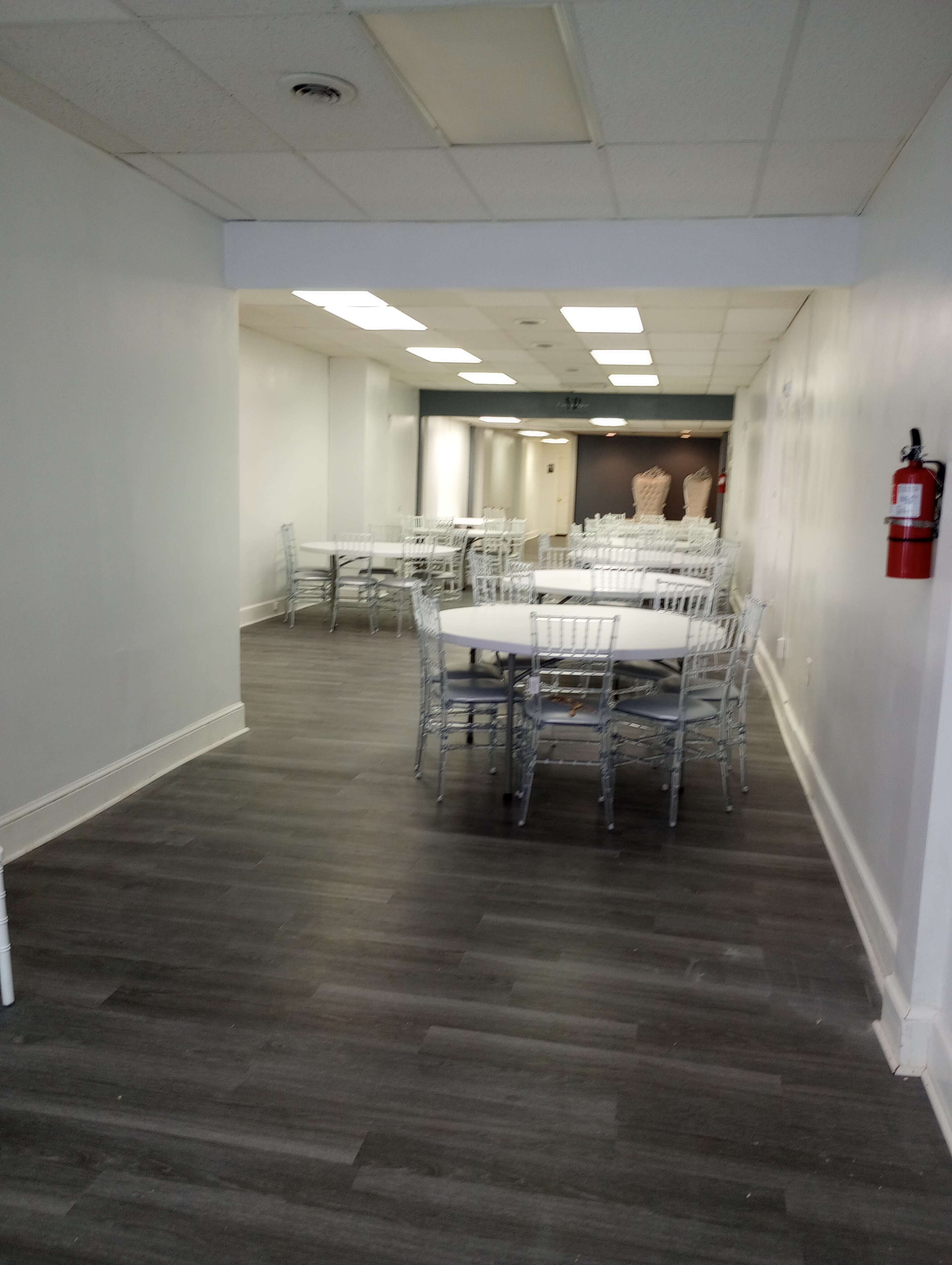 A long, narrow room with several tables and chairs arranged throughout, featuring a clean, modern design and muted colors.