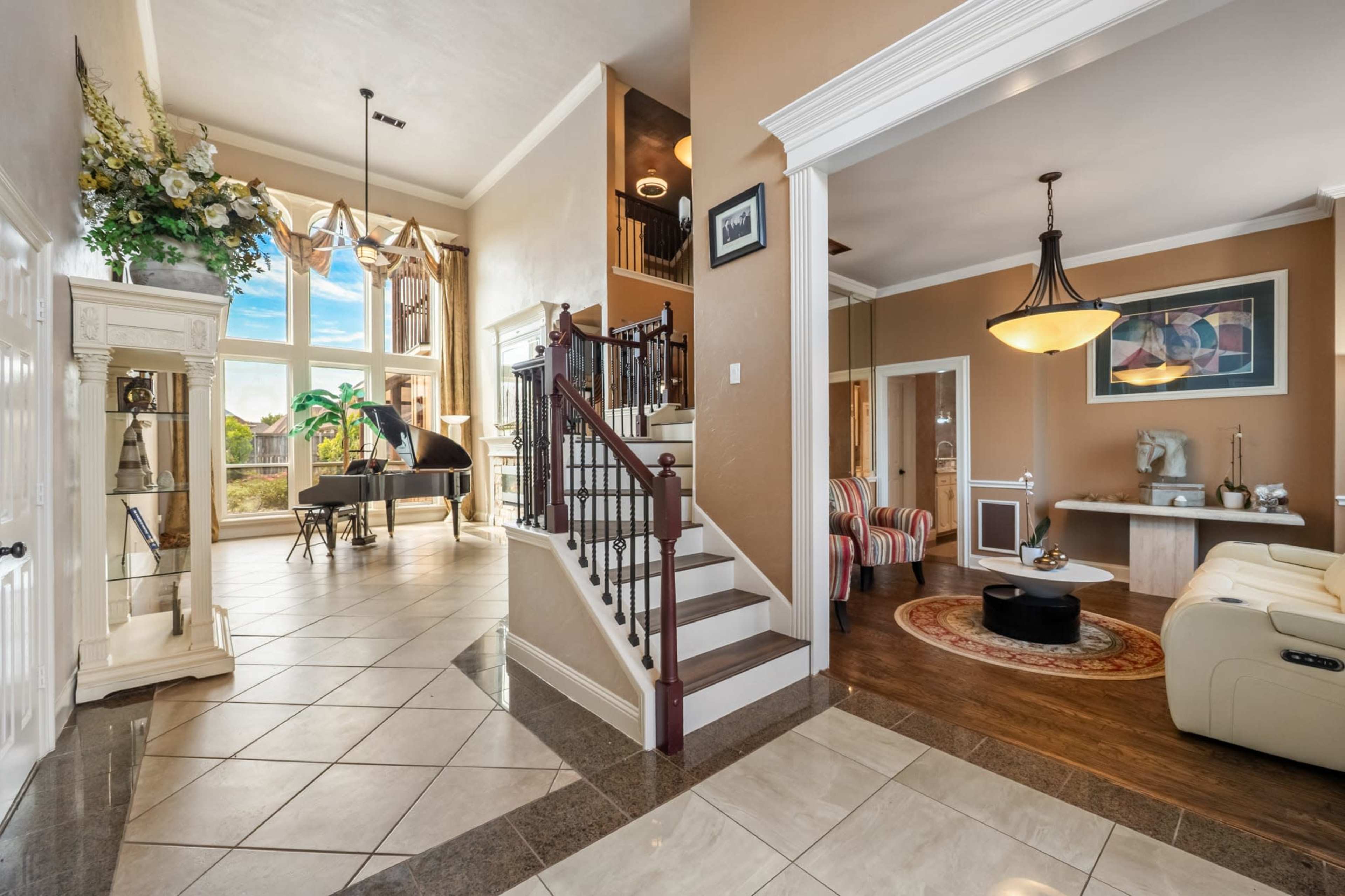 The image shows an elegantly designed entryway leading to a spacious living room with a piano and large windows.