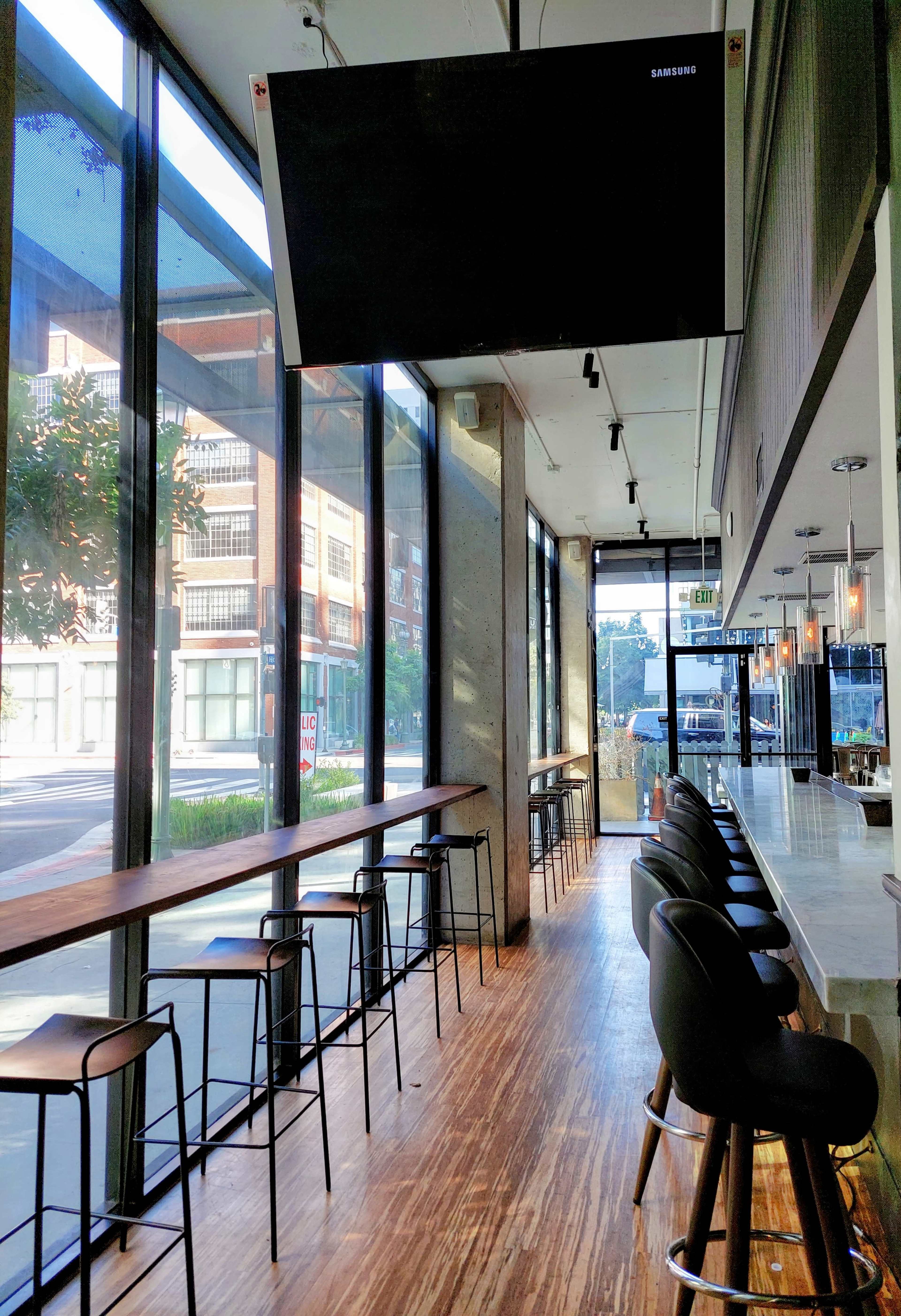 A modern cafe interior with high chairs along a long bar facing large windows that overlook a street.