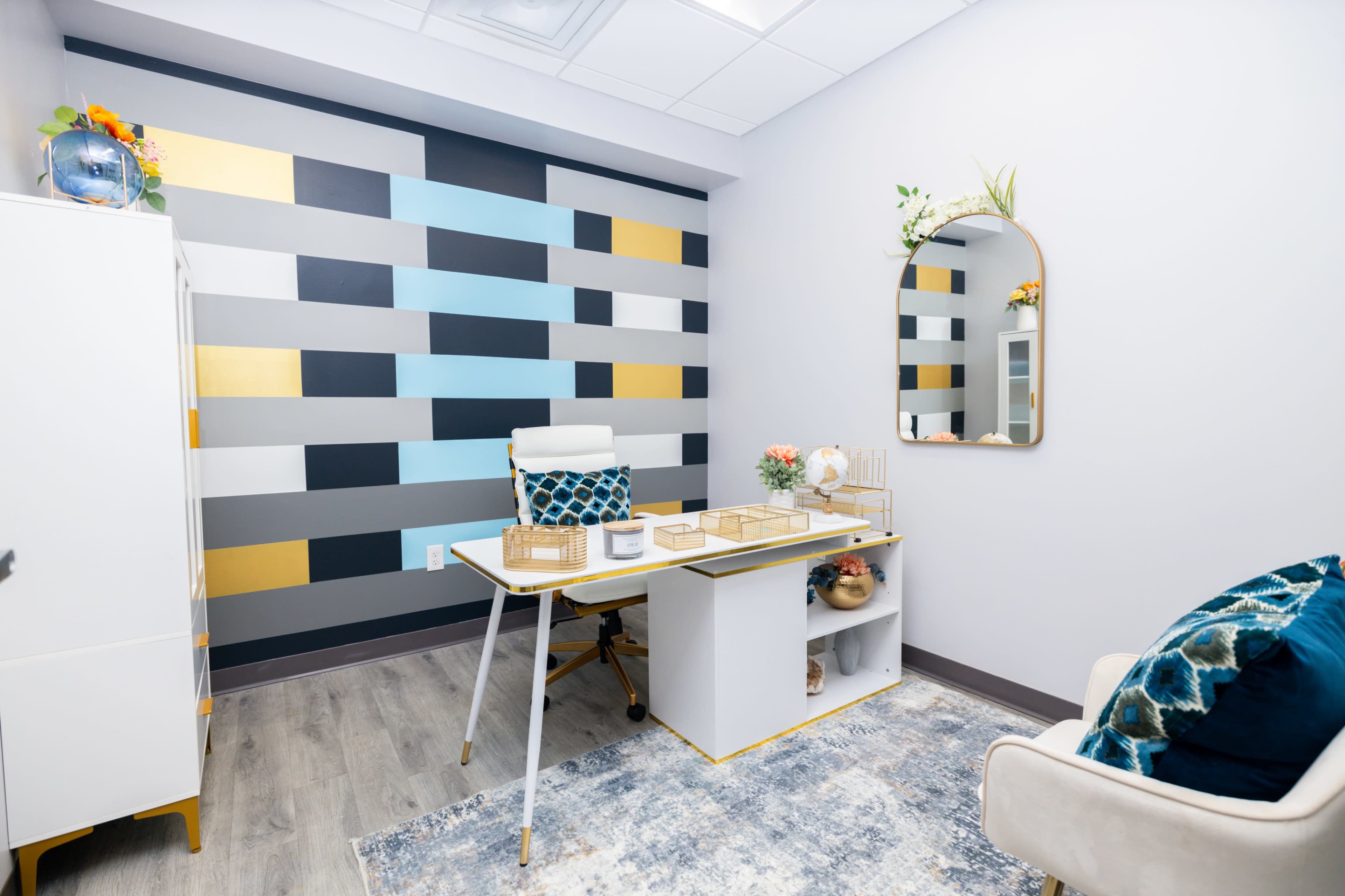 The image shows a modern office space featuring a desk, a mirror, and a colorful striped accent wall.