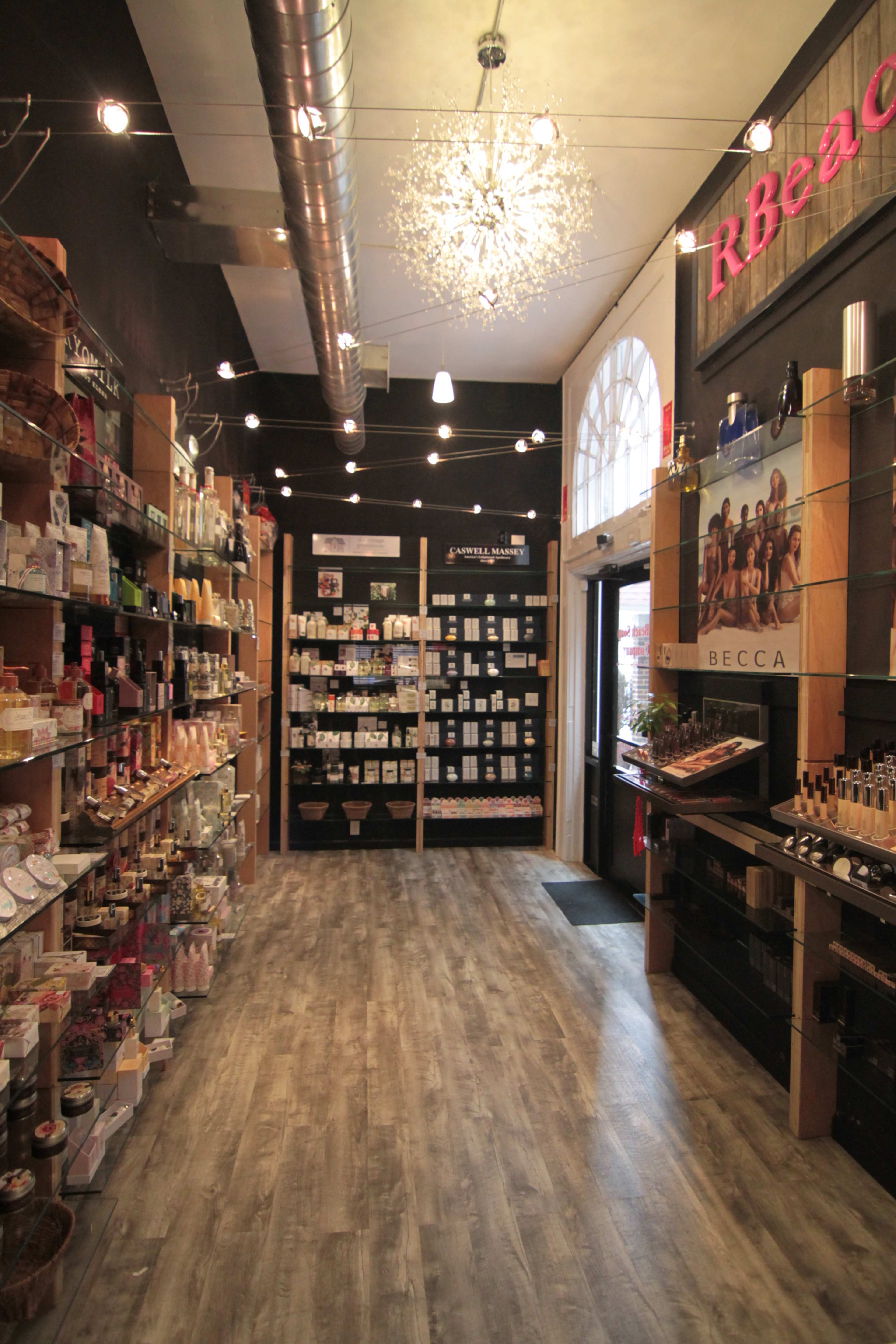 The interior of a retail store features wooden shelves lined with various beauty and personal care products, illuminated by string lights overhead.