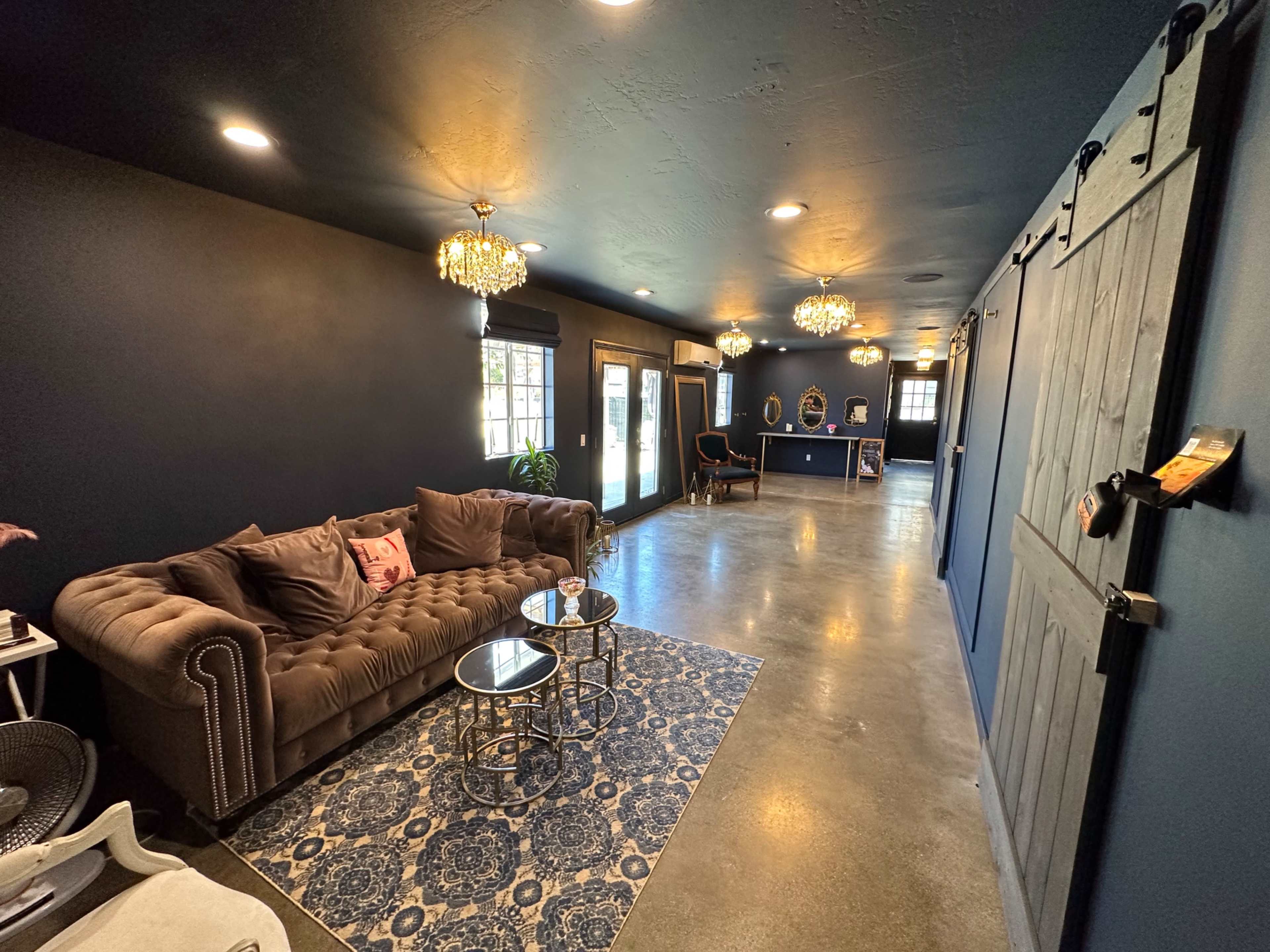 A dark blue room with a plush brown couch, two glass-top tables, a patterned rug, and a sliding barn door.