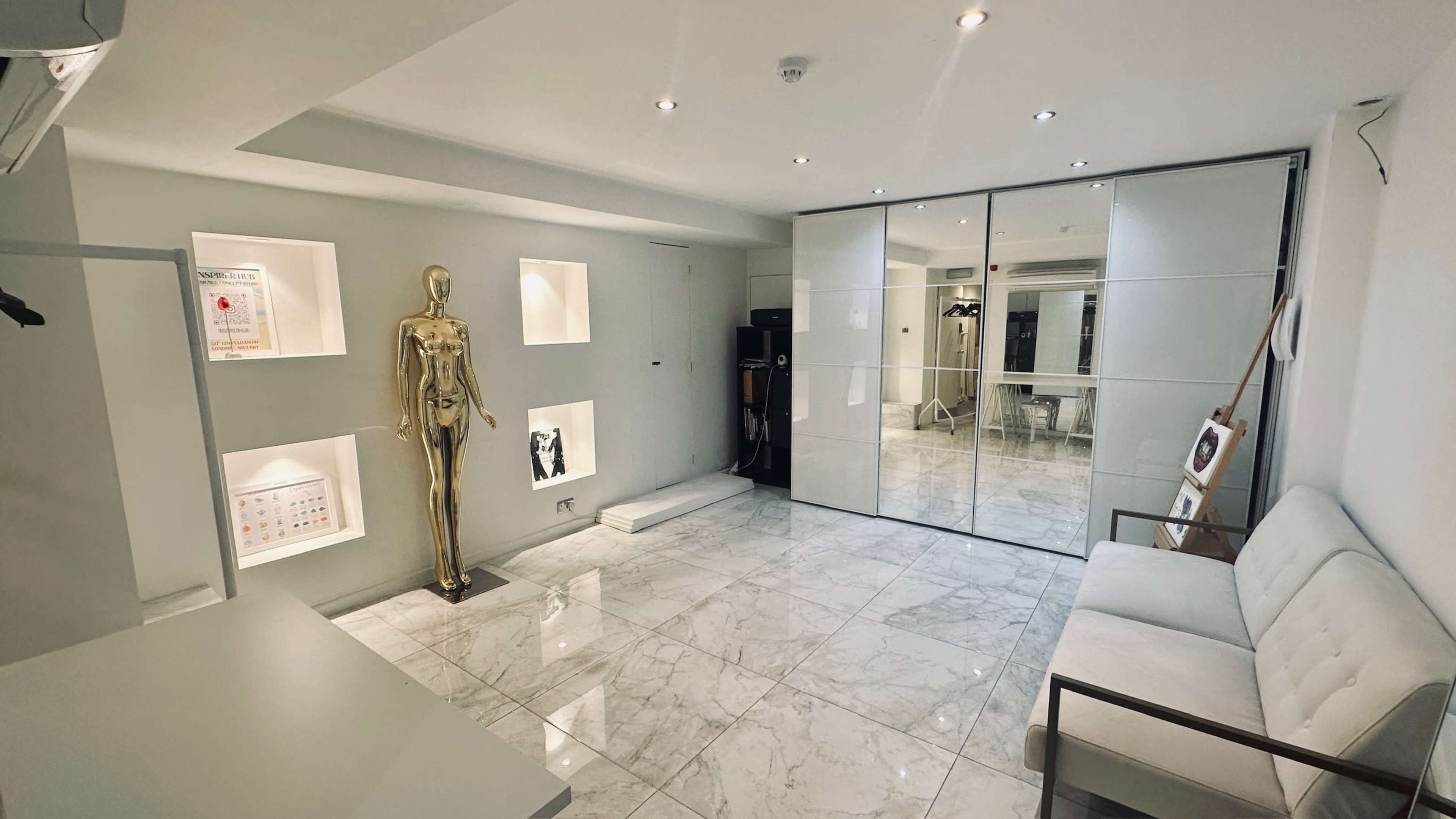 The image shows a modern, minimalist room with marble flooring, a gold mannequin, and mirrored walls reflecting various design elements.