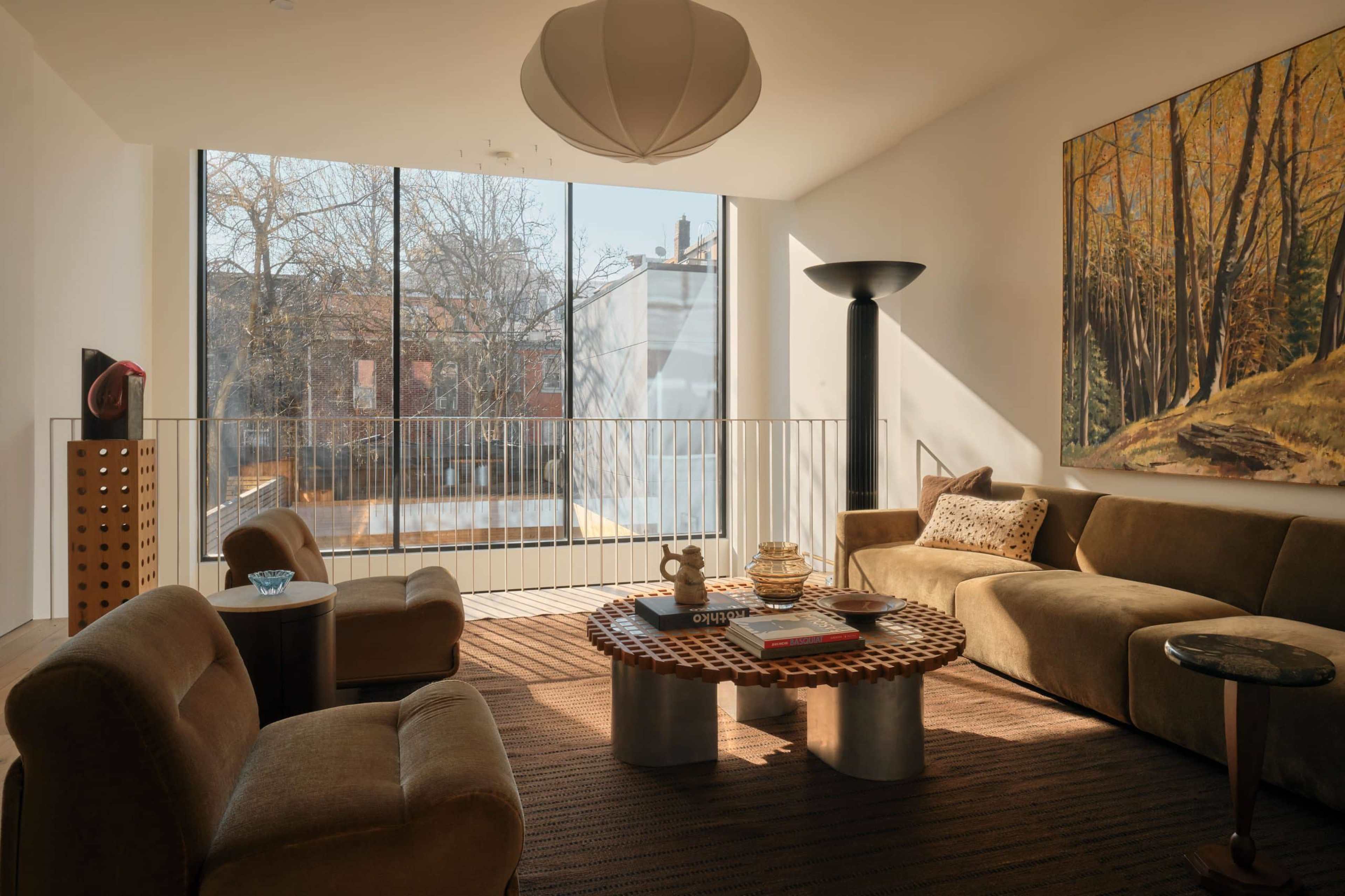 The image depicts a modern living room with large windows, a round coffee table, and a sofa set, complemented by artwork on the wall.
