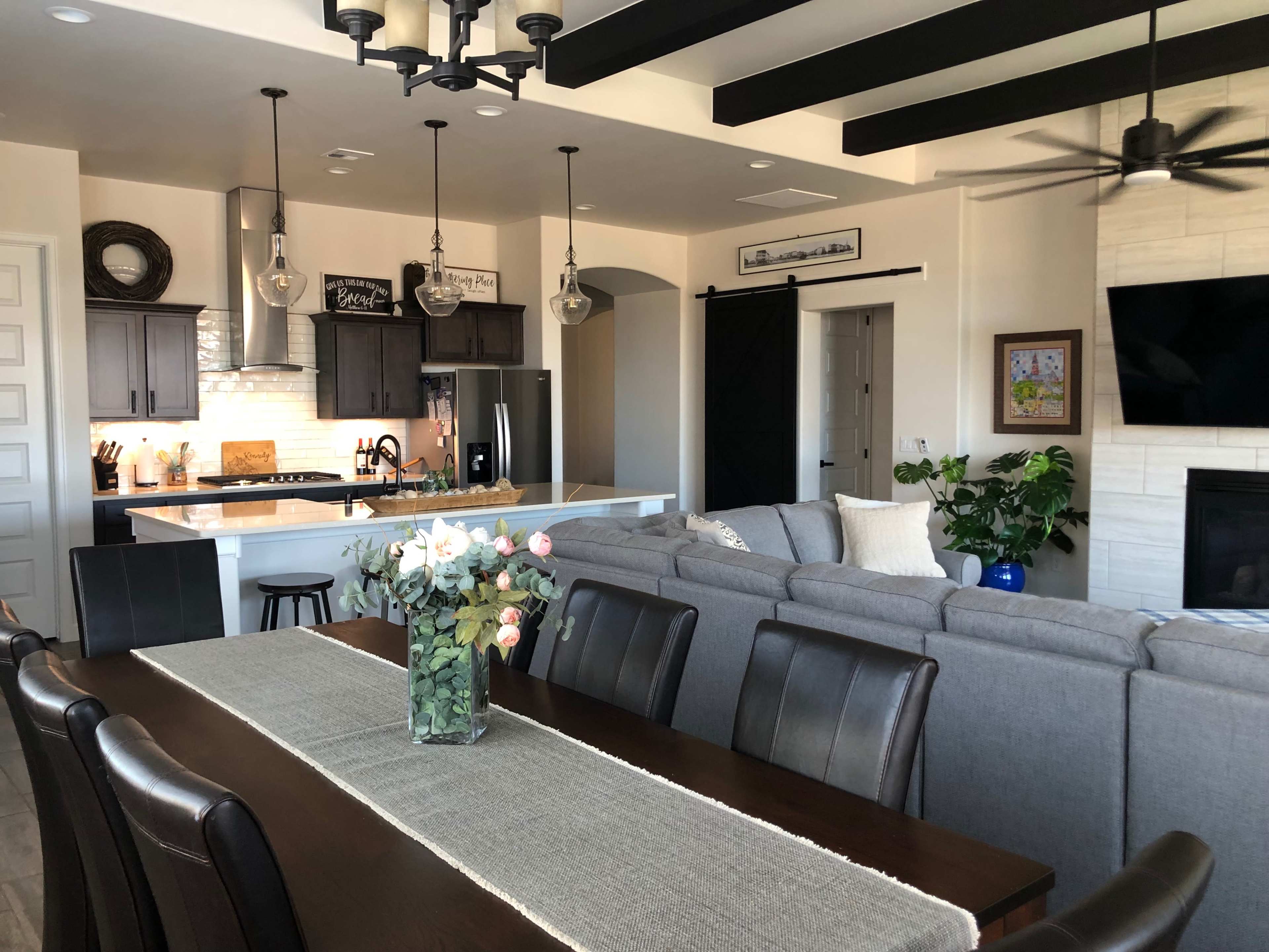 The image shows a modern open-concept living space with a dining table, kitchen area, and a living room featuring a television and a fireplace.