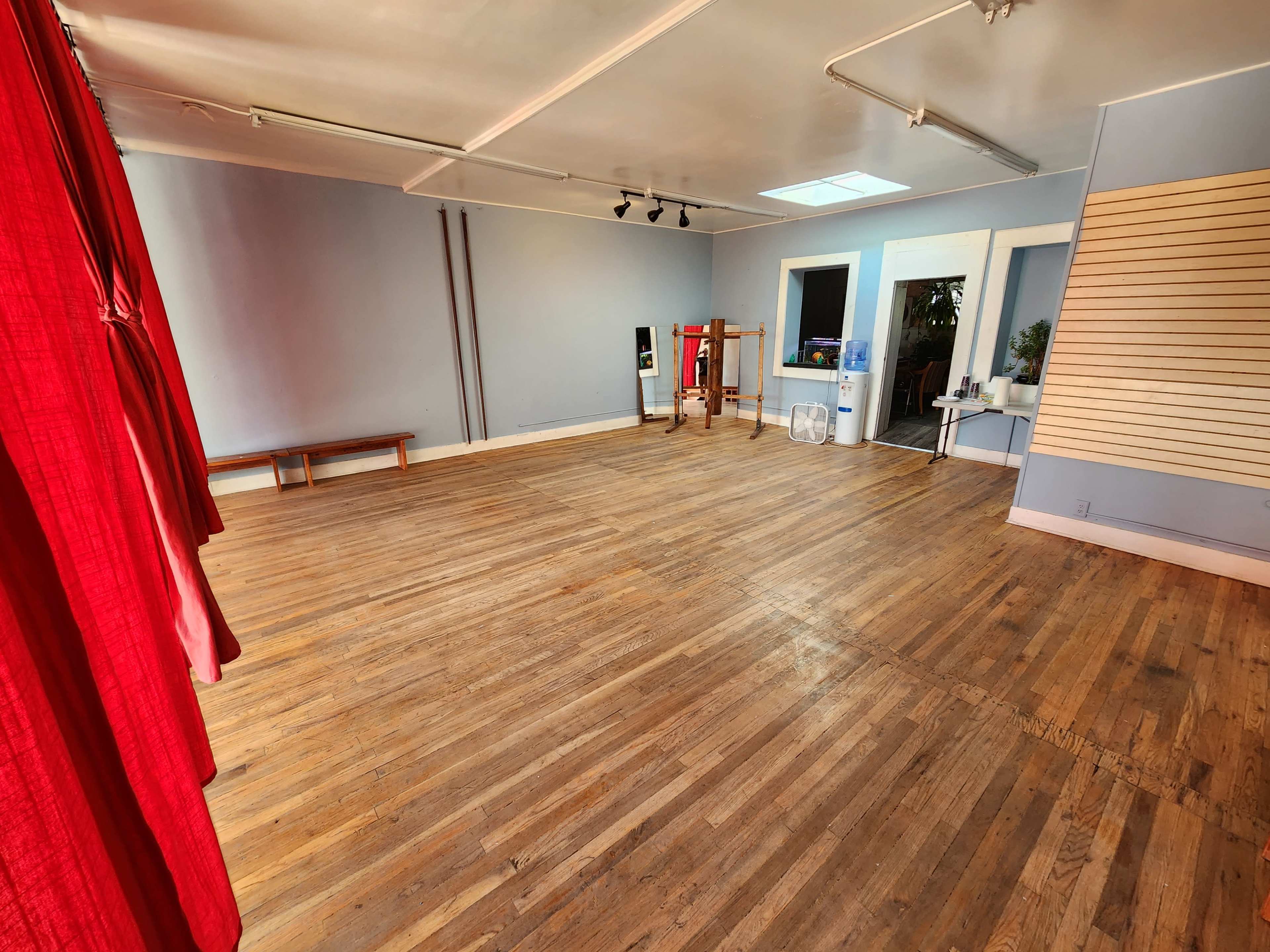 The image shows an empty room with wooden floors, light blue walls, and red curtains on one side.
