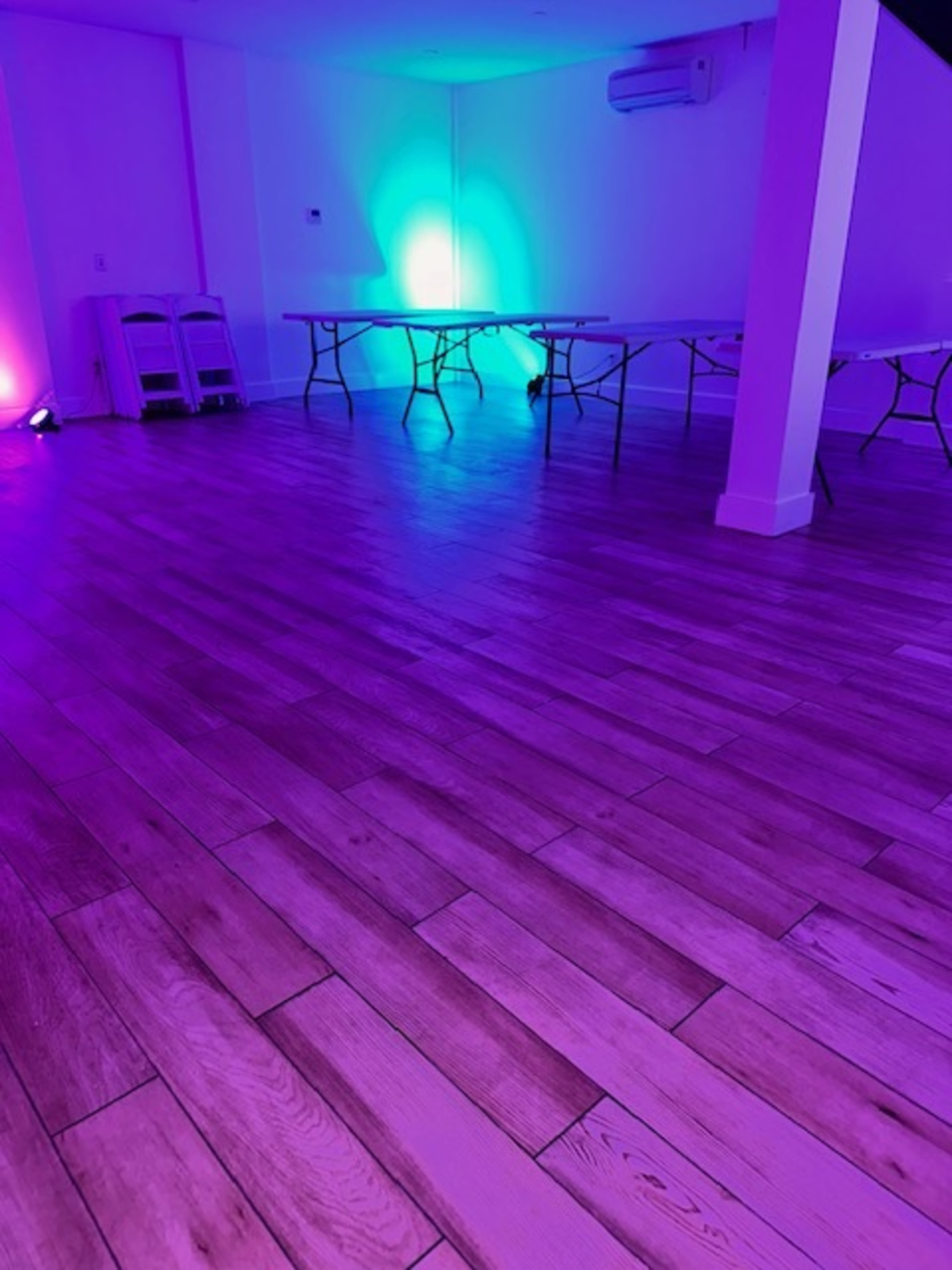 A room with purple and blue lighting, featuring several folding tables arranged on a wooden floor.