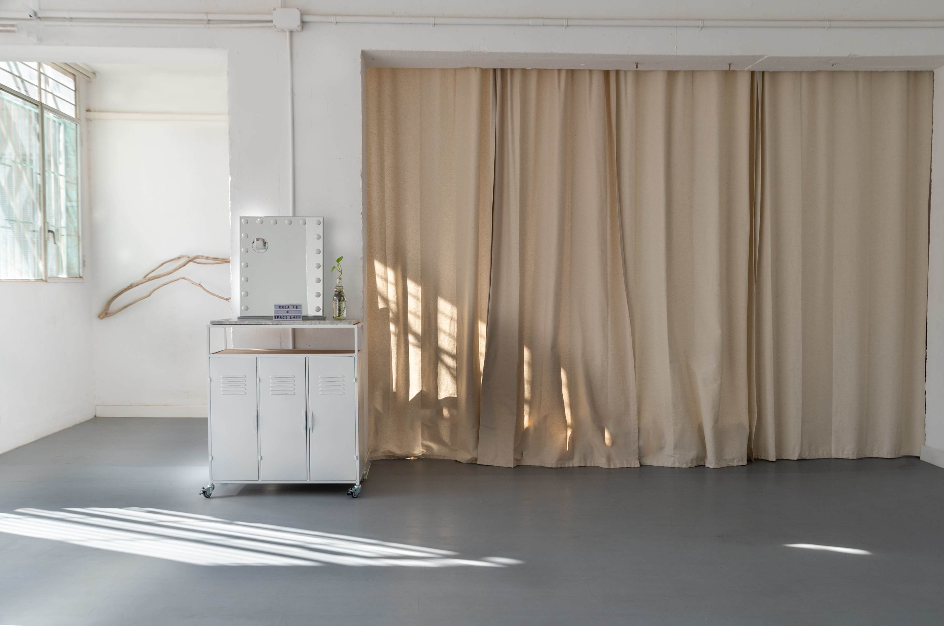 A spacious room with a wooden floor, a curtain draped across an opening, and a white storage cabinet with a mirror next to it.