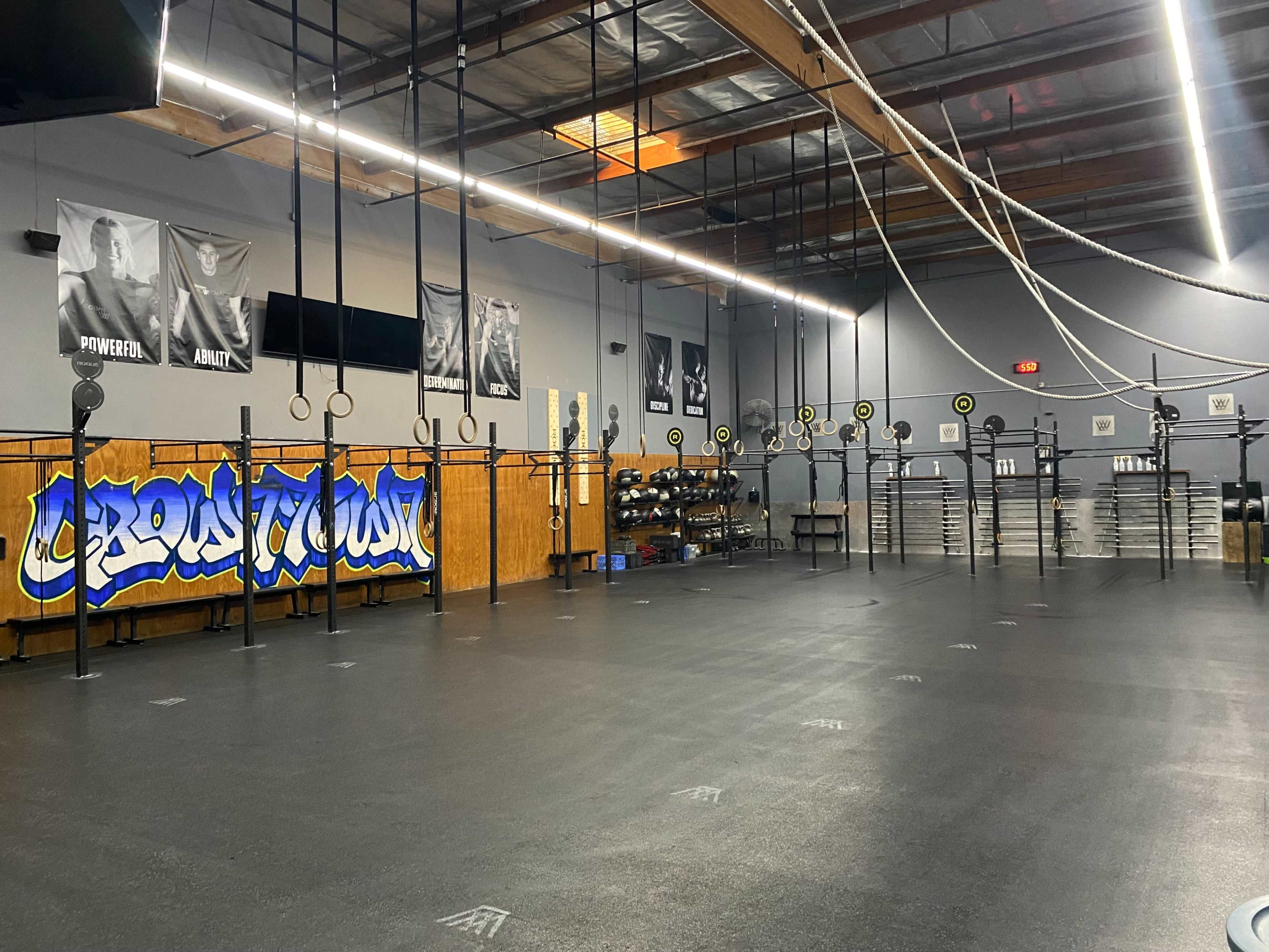 An empty gym with weightlifting equipment, including barbells and plates, against a mural and motivational posters on the walls.