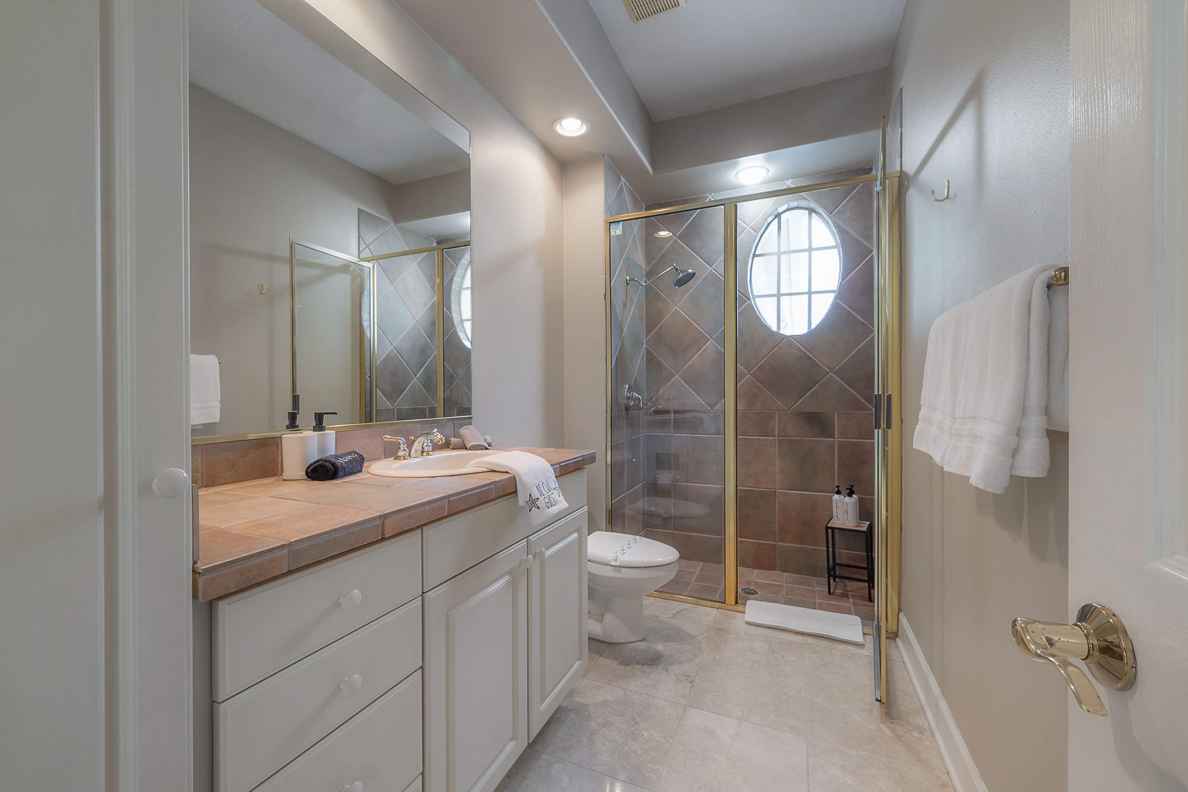 A bathroom featuring a glass shower enclosure, a white vanity with a sink, and light-colored tile walls and floor.