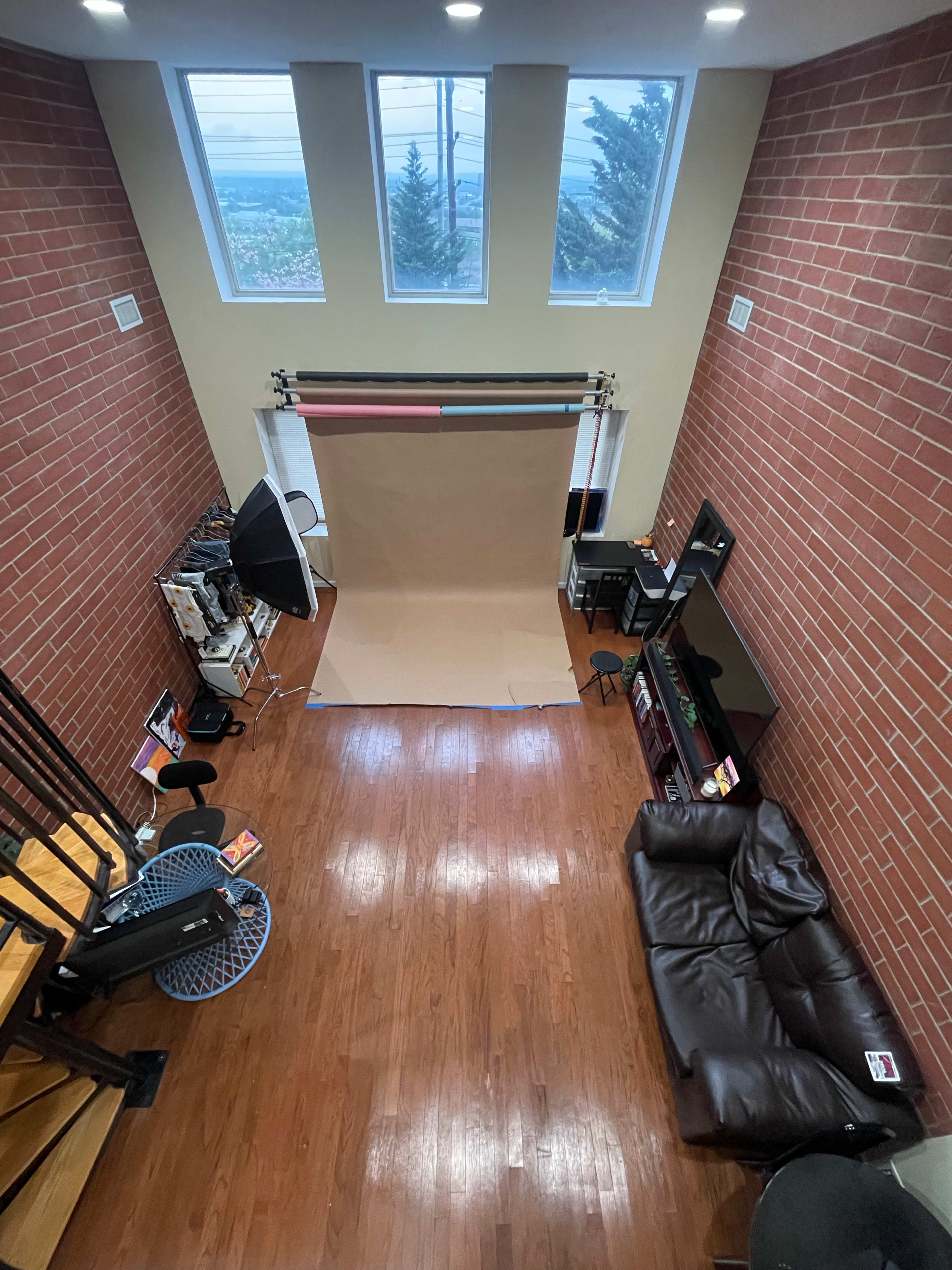 A spacious interior with brick walls, a photography backdrop, a couch, and a staircase leading up.